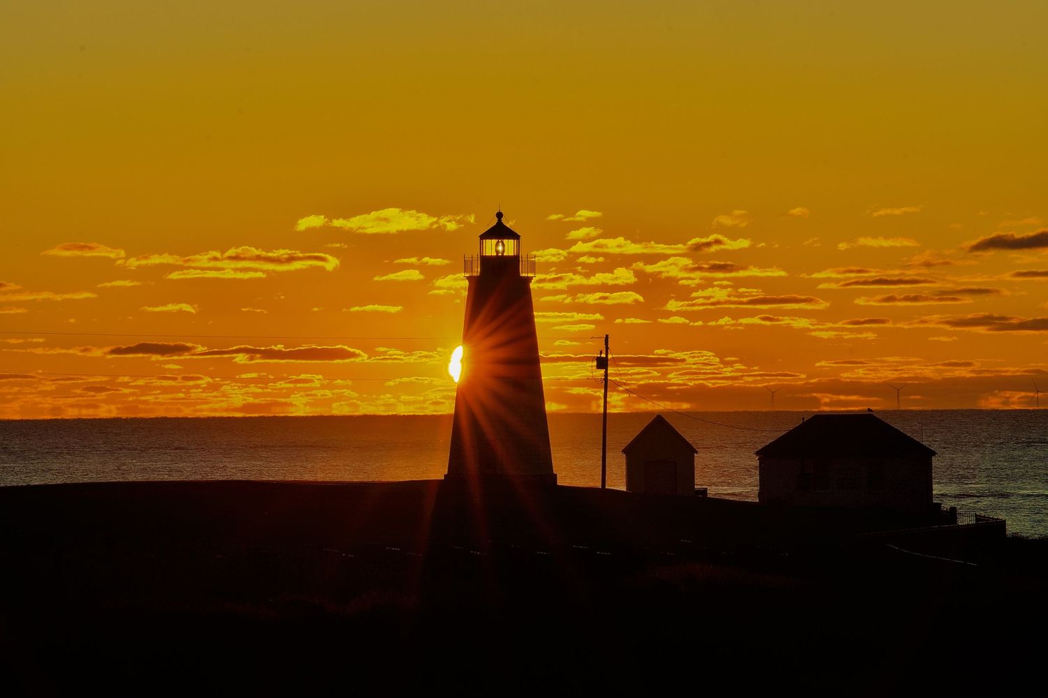 Lighthouse silhouette against a golden orange sunset sky with dramatic cloud formations.