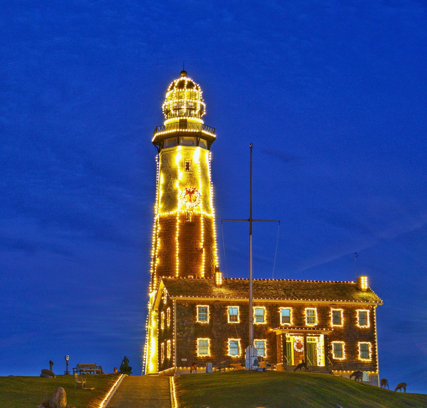 A historic lighthouse illuminated with warm golden lights against a deep blue twilight sky stands majestically on Montauk Point.