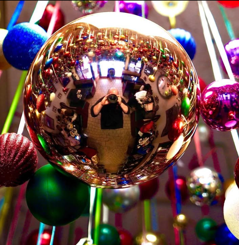 Colorful reflective Christmas ornament baubles hanging with blurred holiday lights in the background.