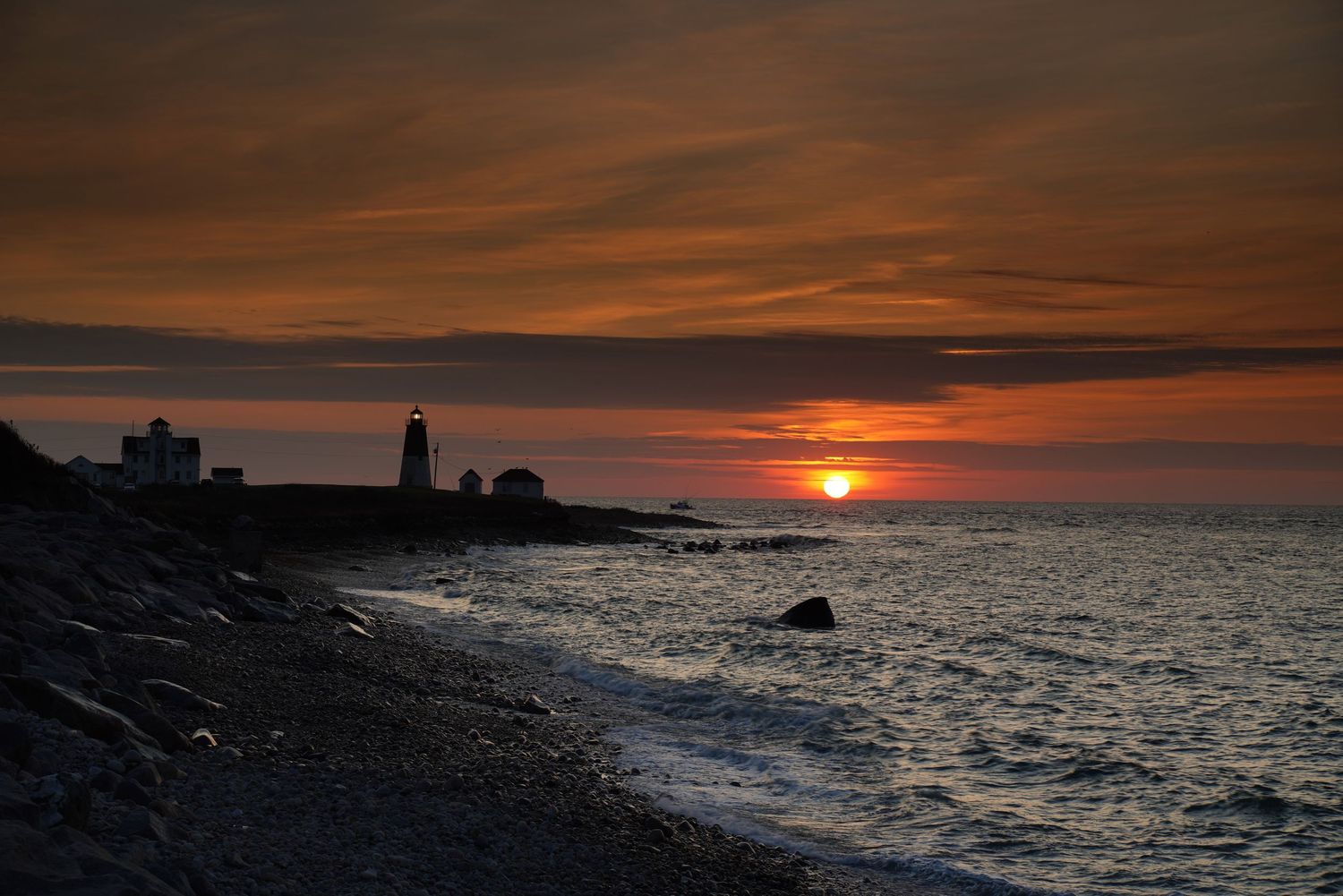A dramatic sunset illuminates the dark ocean waves and coastline with vibrant orange and red hues in the sky.