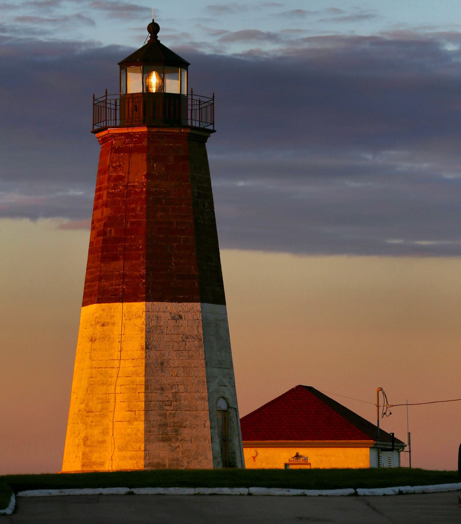 Historic lighthouse tower glows golden in the warm evening light against a dusky sky.