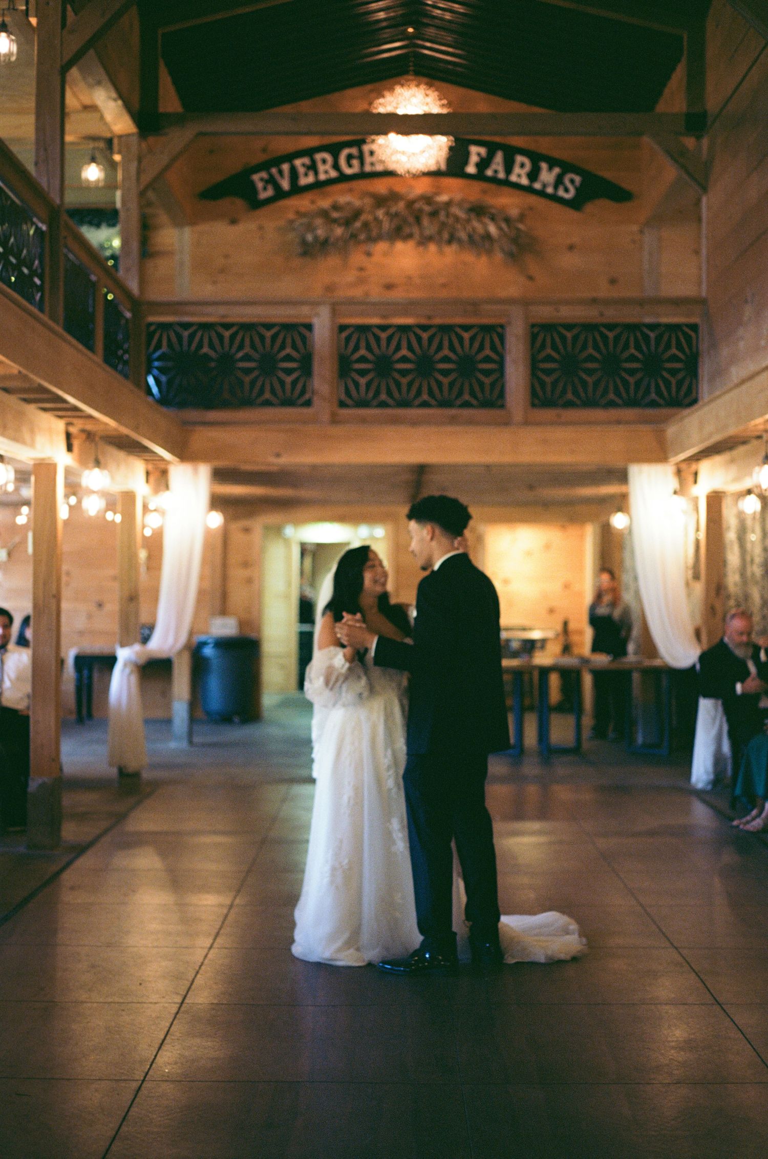 A romantic first dance between newlyweds at Evergreen Farms venue illuminated by warm lighting and white drapes. Color Film.
