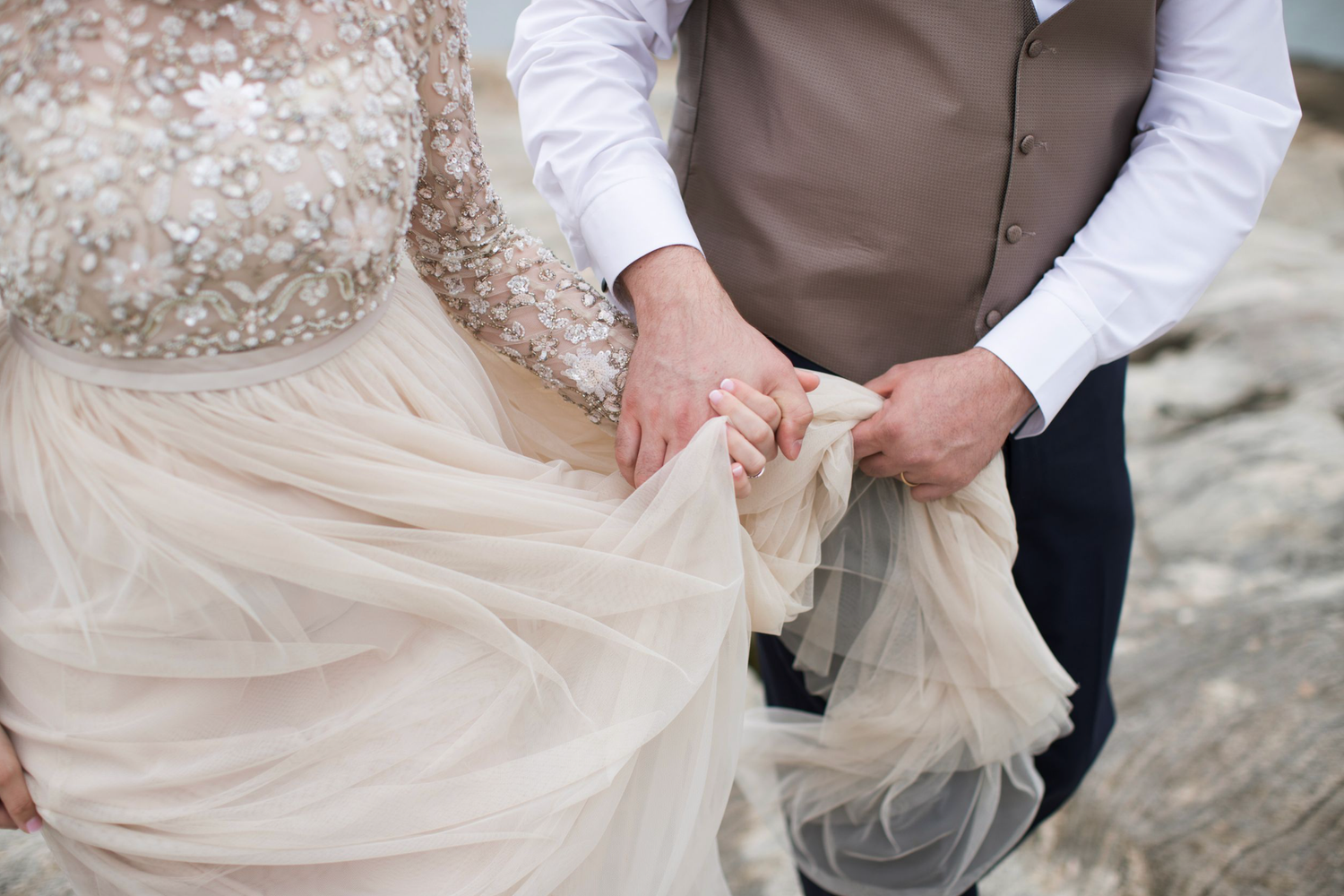Couple in wedding attire holding hands and walking together on a stone wall at the Beach. Madison Connecticut Beach.