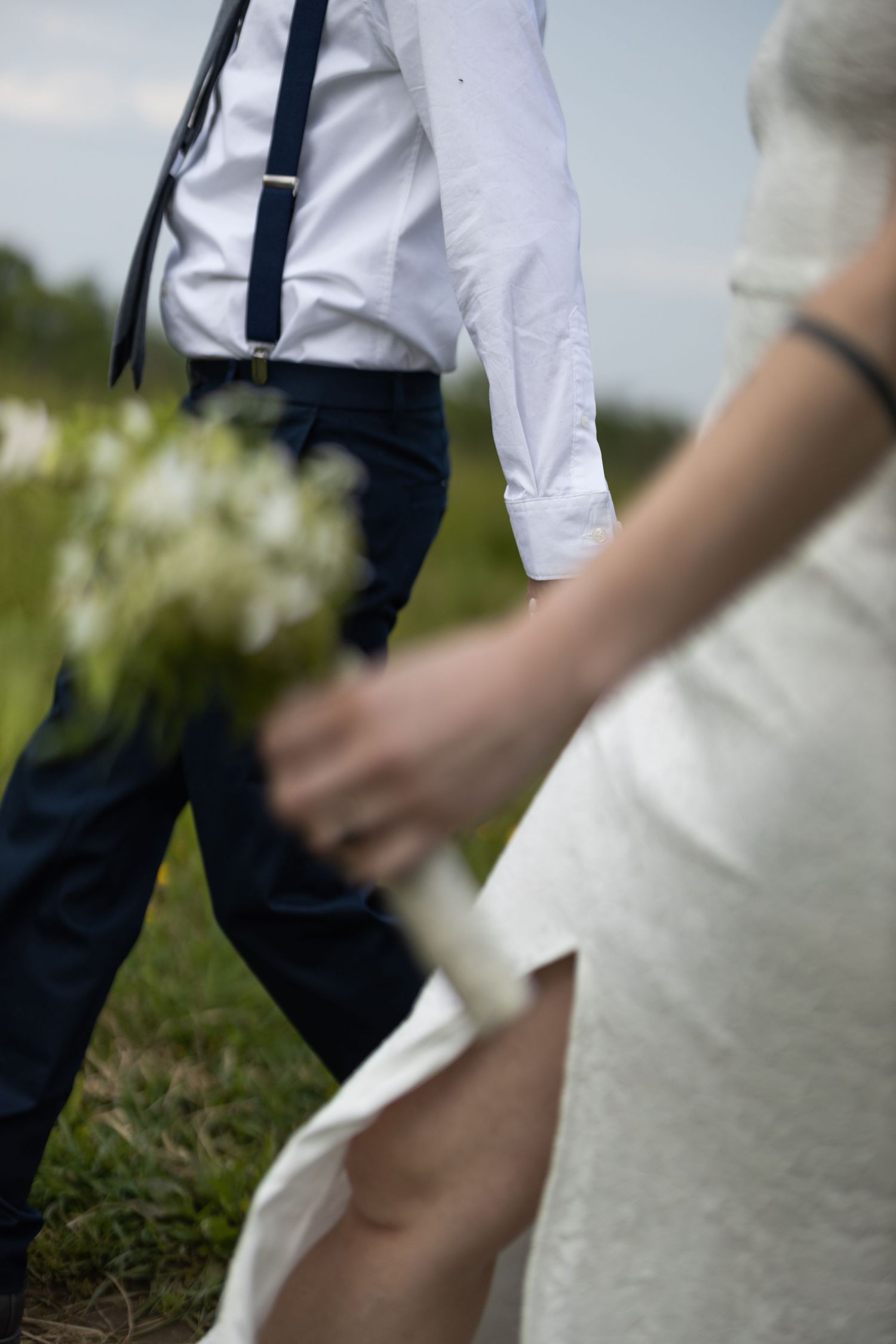 Close-up view of formal attire with navy suspenders and white dress shirt against outdoor wedding setting.