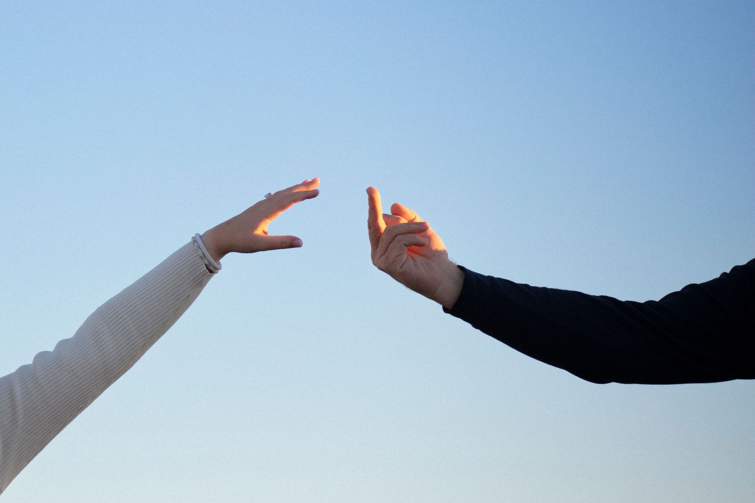 Two hands reaching towards each other against a blue sky, one giving middle finger as a joke. Hilarious photo. Not posed.