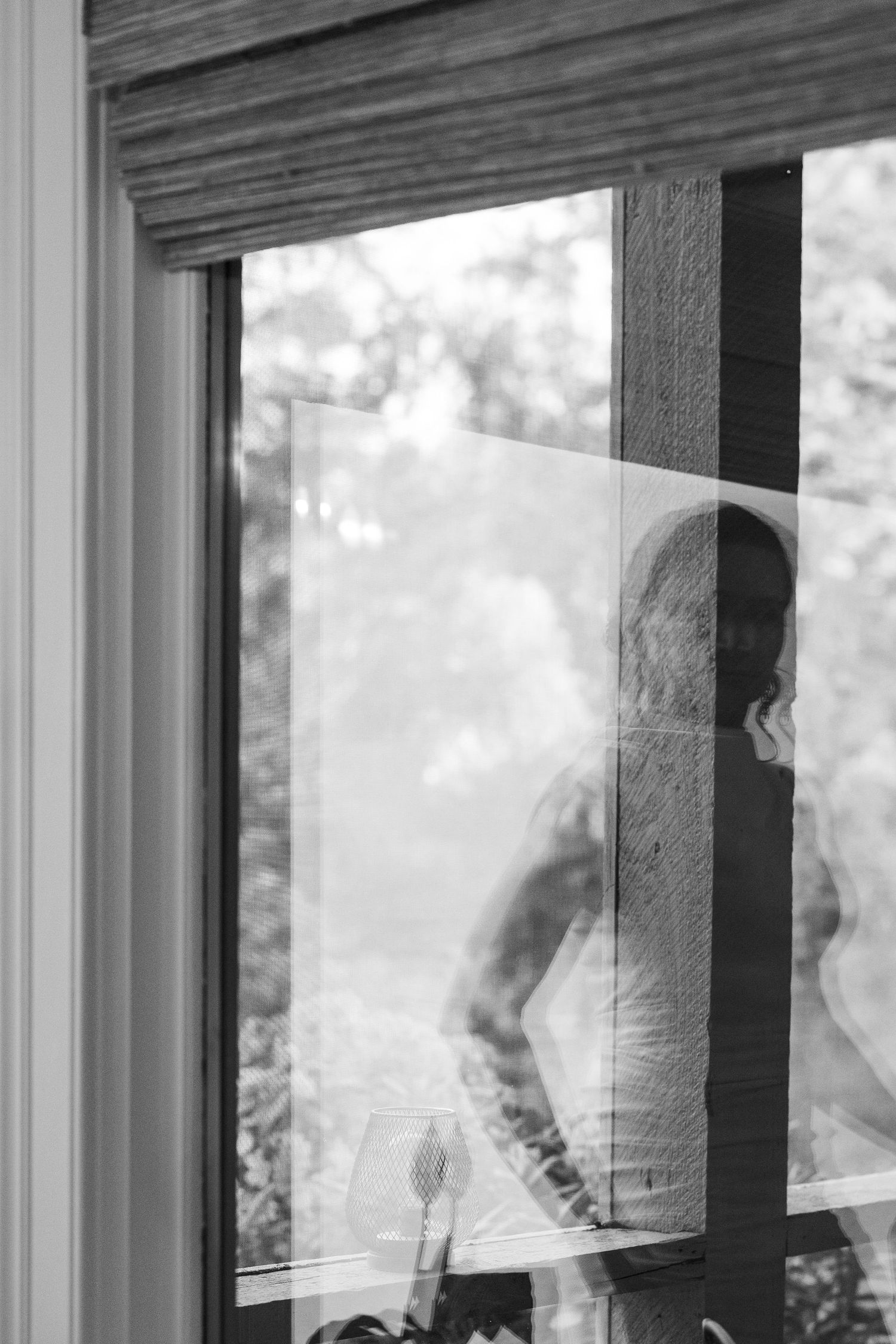 A black and white photograph shows a window with vertical panes reflecting light and casting shadows on the interior.