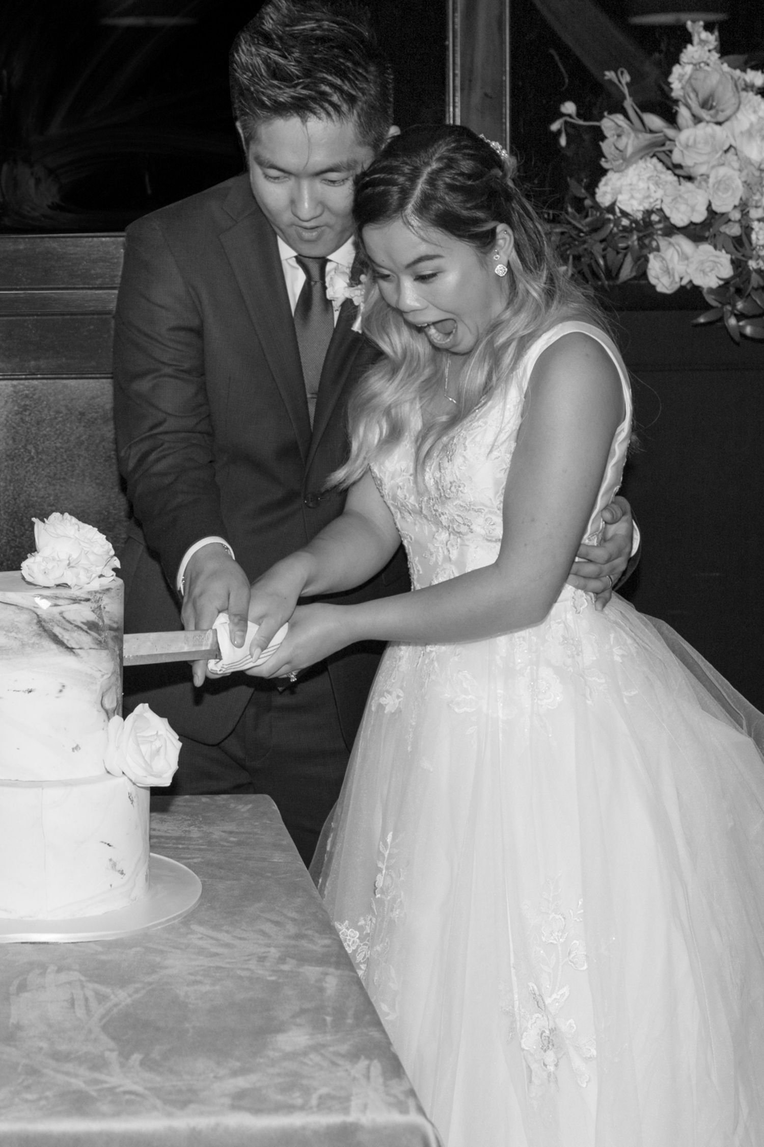 Black and white portrait of bride and groom cutting their cake.