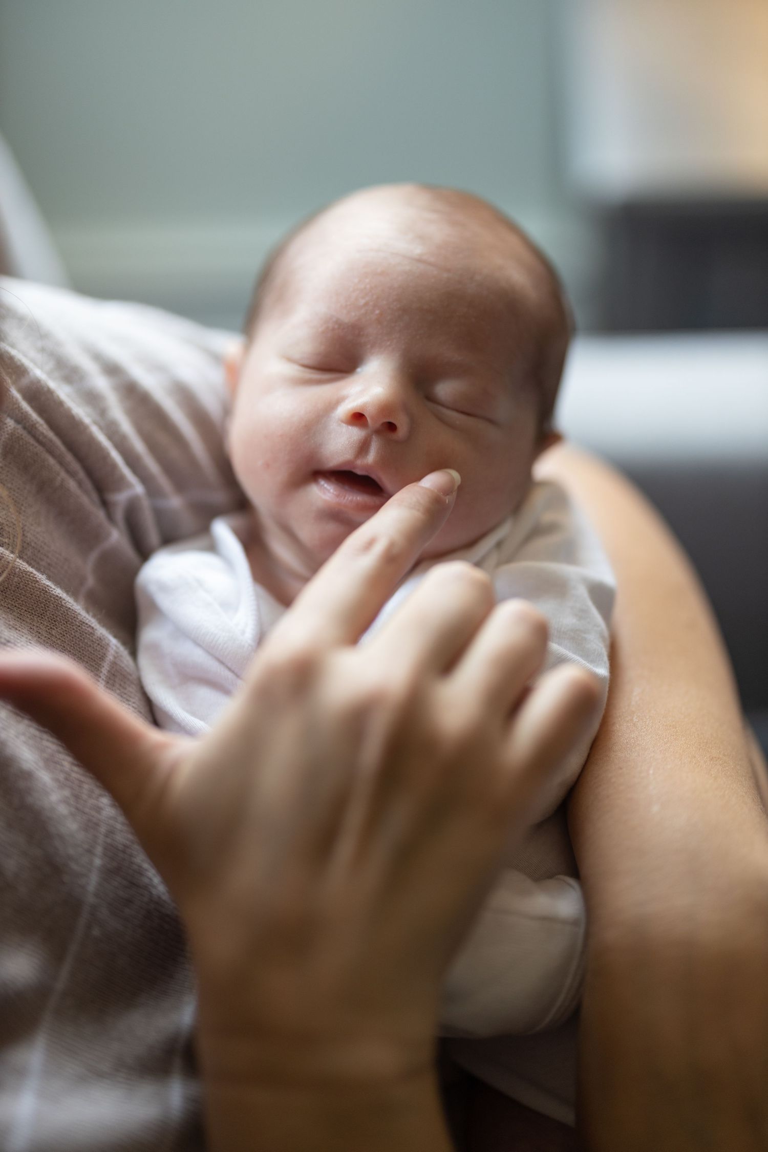 A sleeping baby rests peacefully in soft brown blankets with a tiny hand visible.