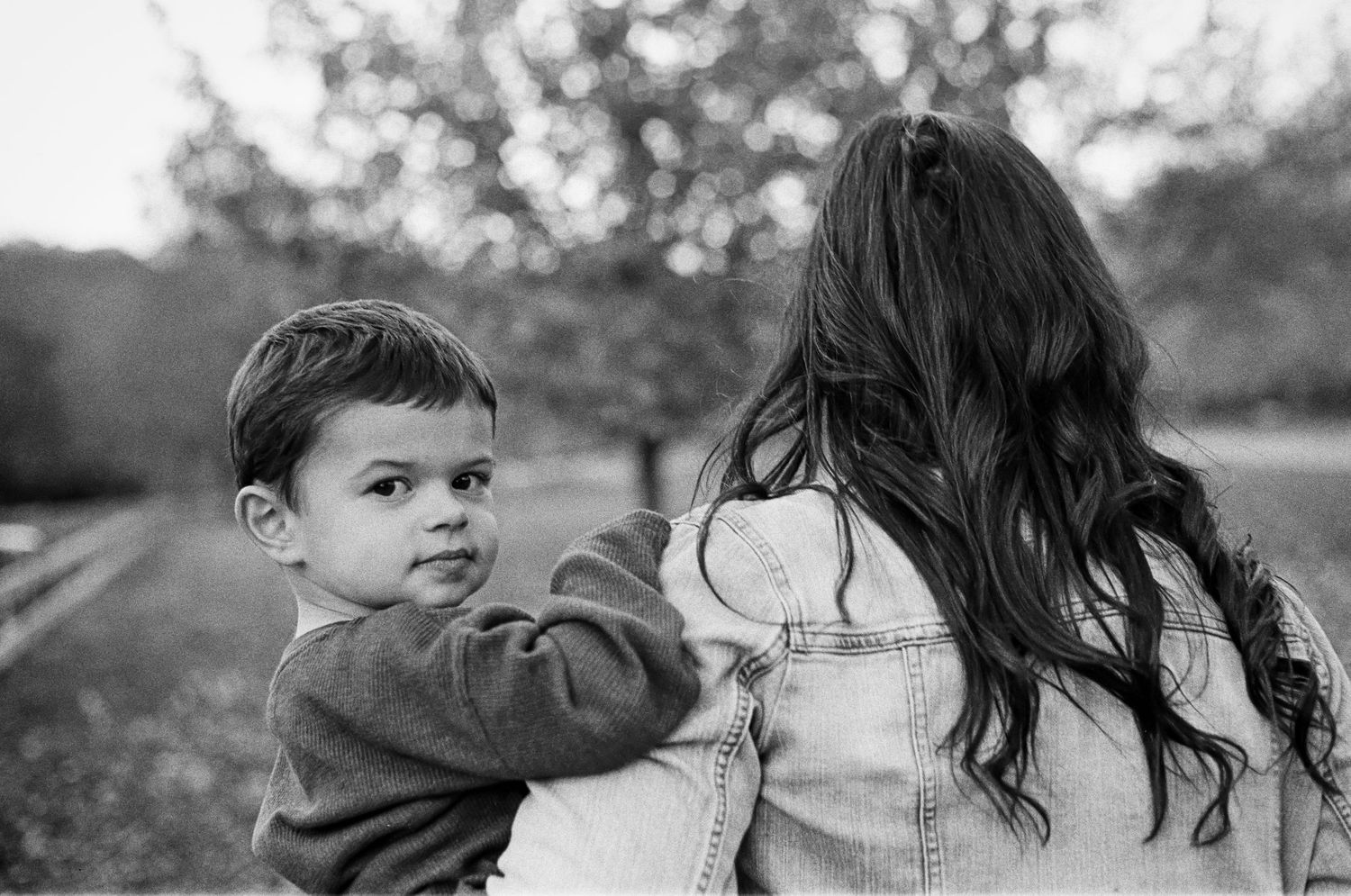 Black and White Film Portrait a mother holding child. Child is looking right at me with slight Smile.