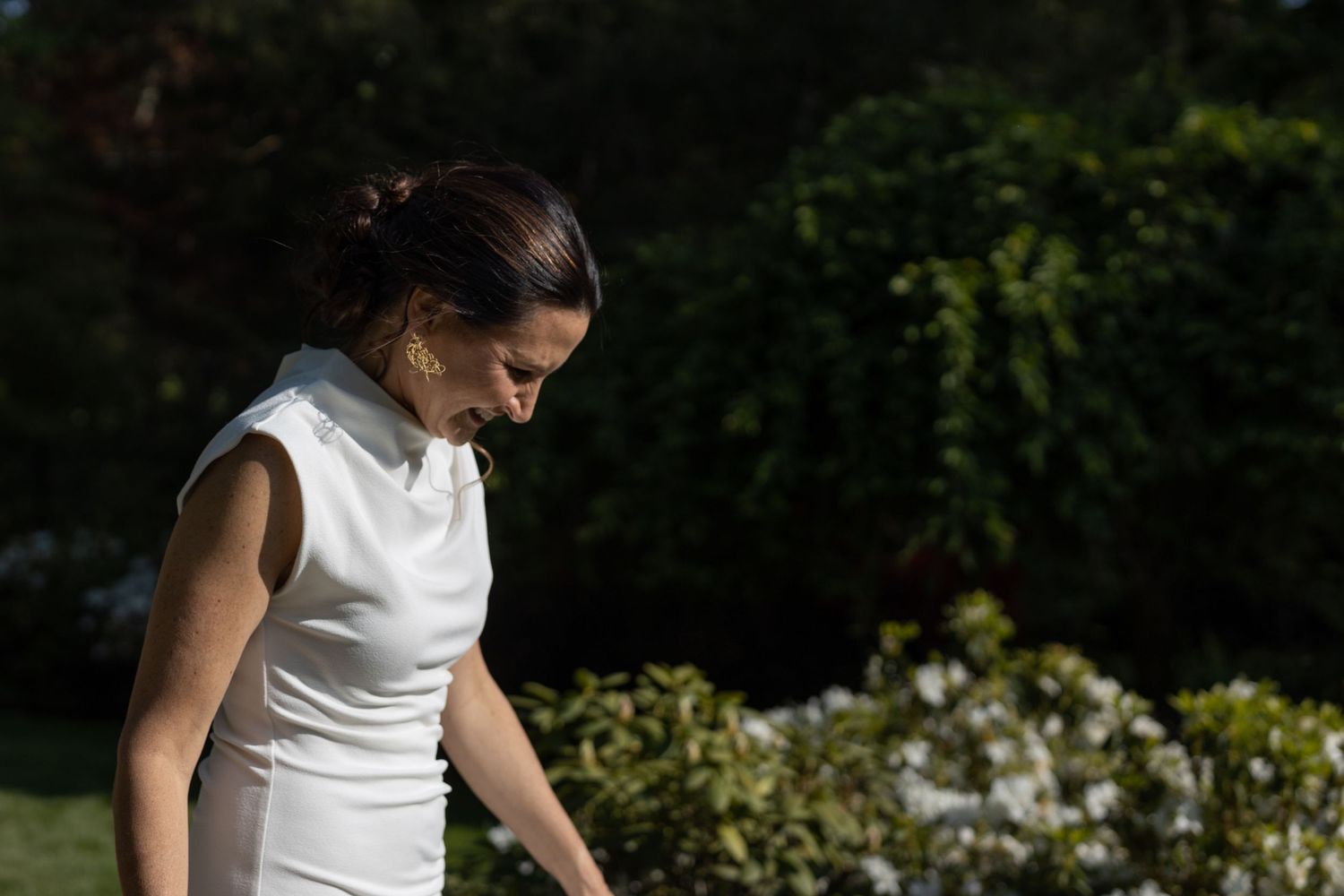 A bride in a white dress walks through a sunlit garden setting during a wedding photoshoot.