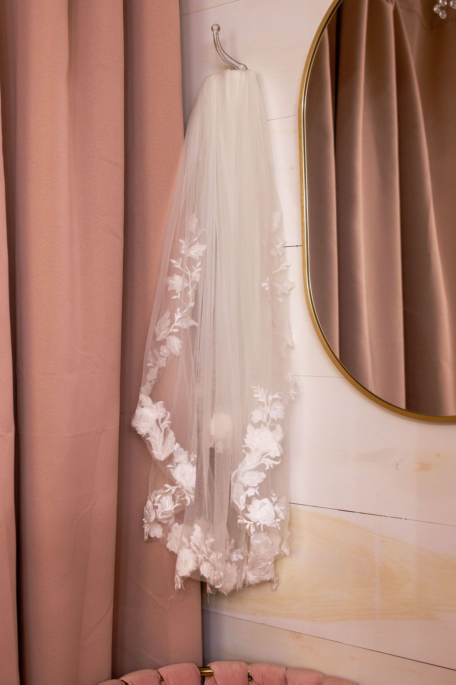 Close-up view of delicate white floral appliques on sheer tulle wedding dress fabric against a blush pink background.