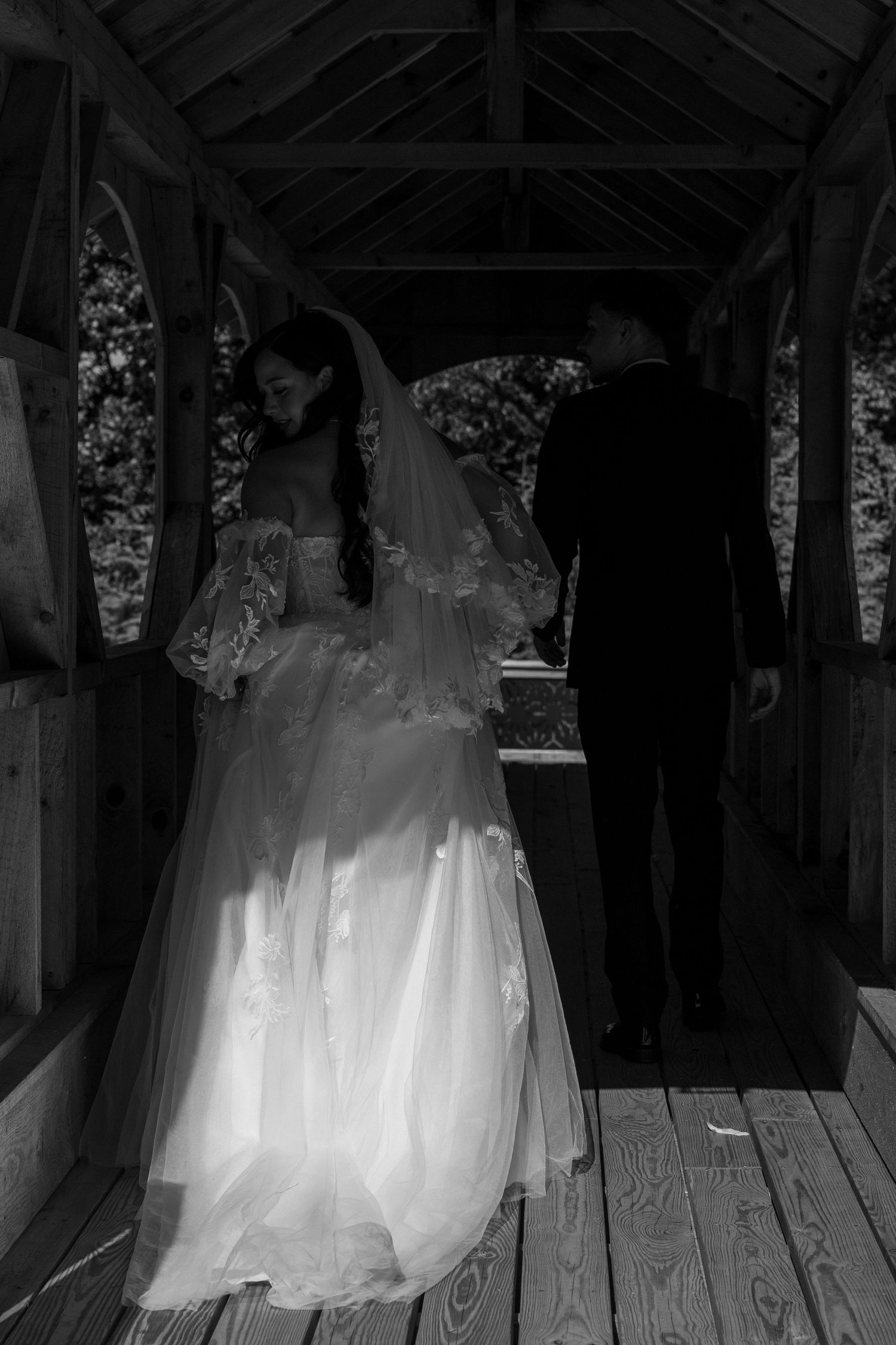Black and white portrait of Bride and groom walking on the covered bridge.