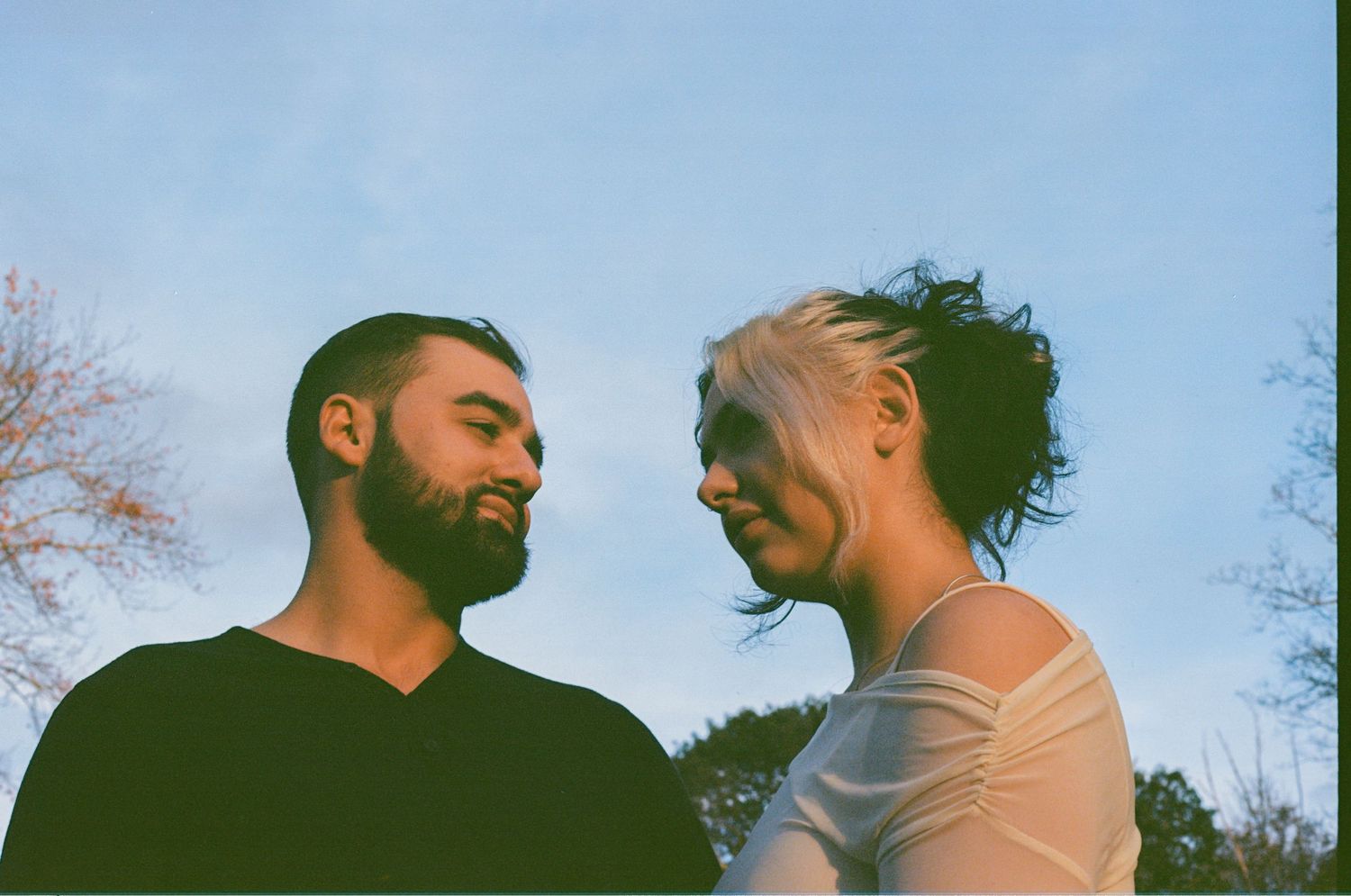 portrait of a couple gazing at each other outdoors under a blue sky, in a romantic couple portrait.
