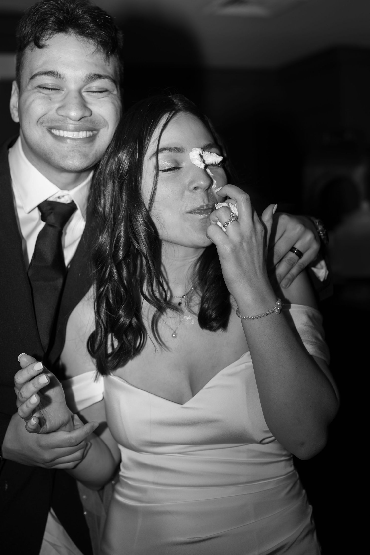 Black and white photo of a smiling groom embracing his emotional bride during their wedding reception dance.