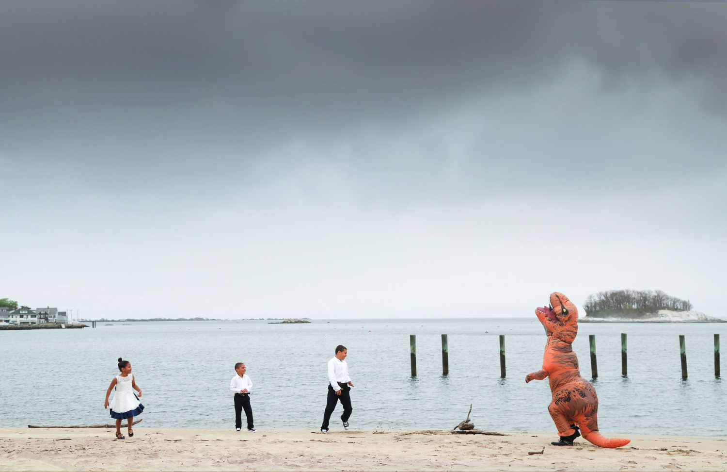 A panoramic view of a foggy beach with wooden posts and people in orange clothing walking along the shoreline.