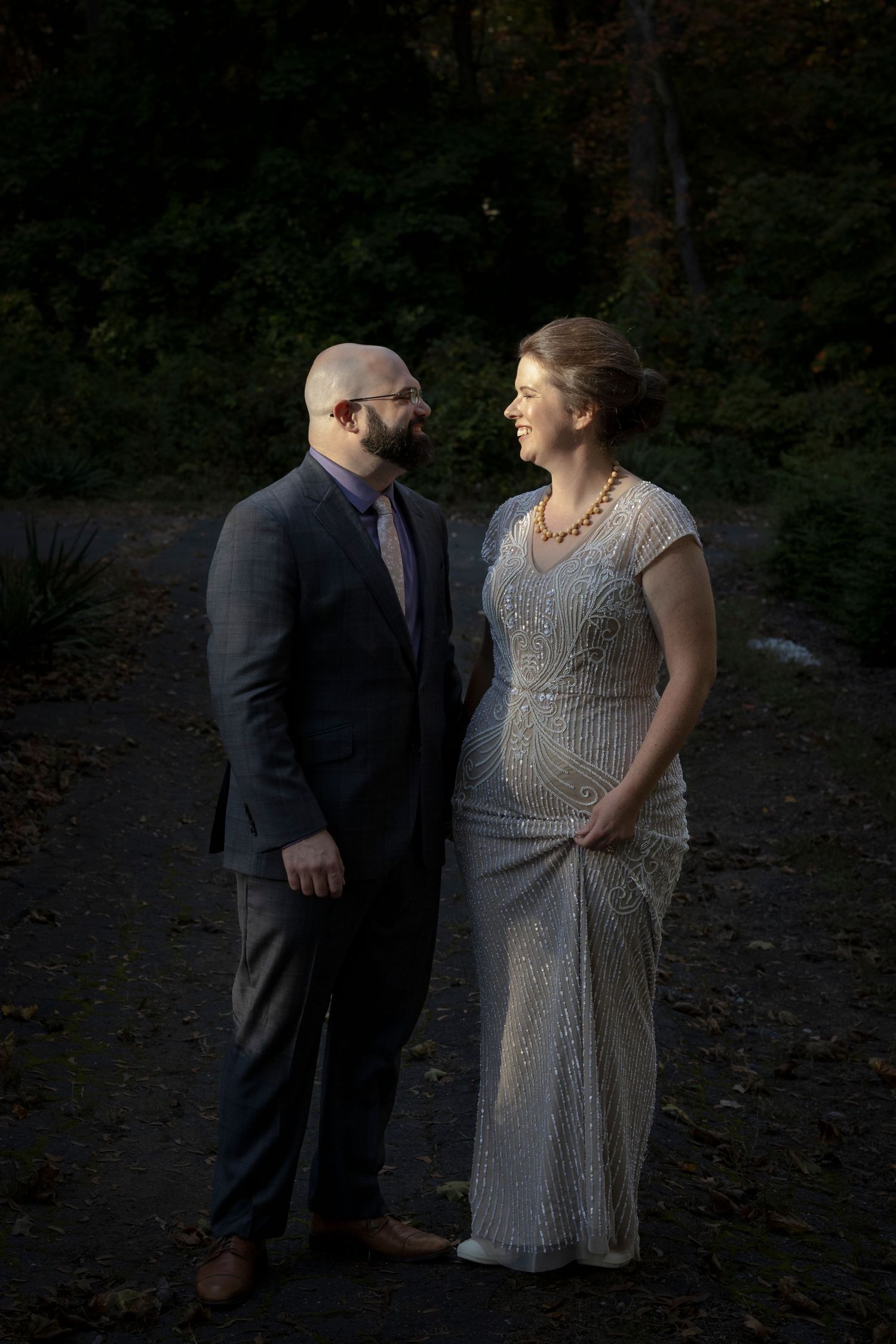 A couple in formal attire shares a romantic moment in a wooded outdoor setting at dusk. moody couples portrait.