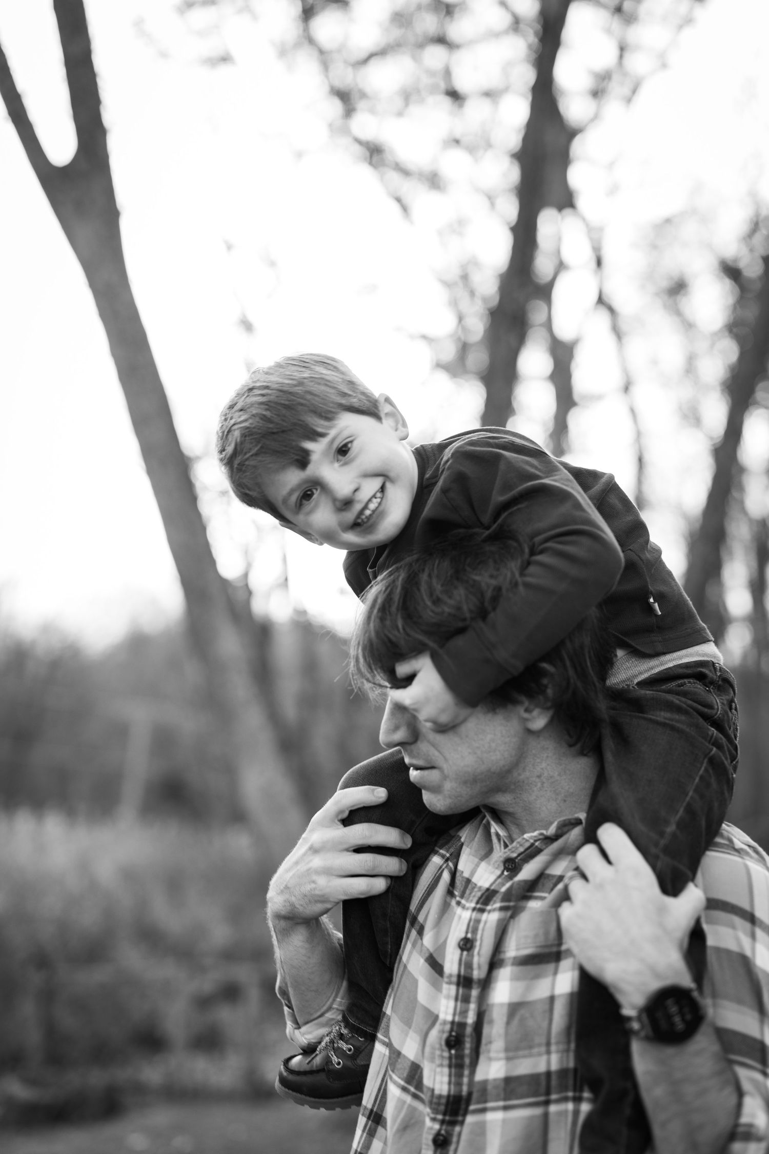 A heartwarming black and white portrait of a child riding on his dads shoulders outdoors in a natural setting.