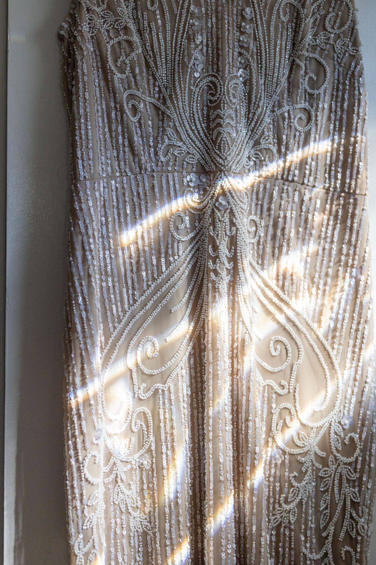 Close-up of intricate beaded embroidery pattern on wedding dress fabric with sunlight creating dramatic light and shadow effects.