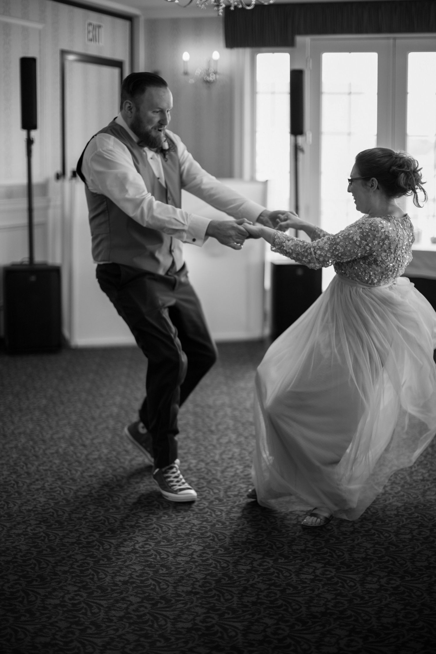 A couple dances joyfully at their wedding reception, with the bride wearing a flowing white dress and groom in a vest.