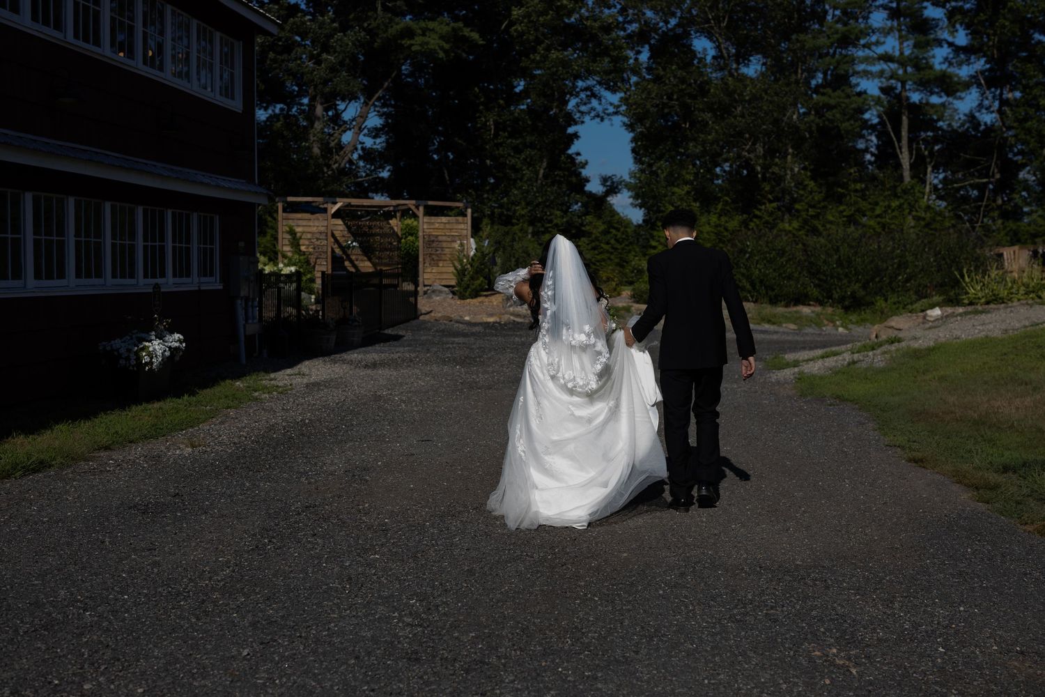 A bride and groom walk down a rural road together on their wedding day. Moody direct sunlight.