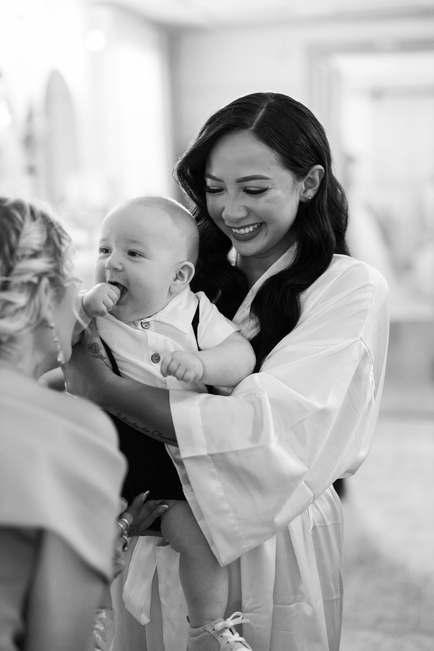 Black and white portrait of a bride laughing while holding a baby.