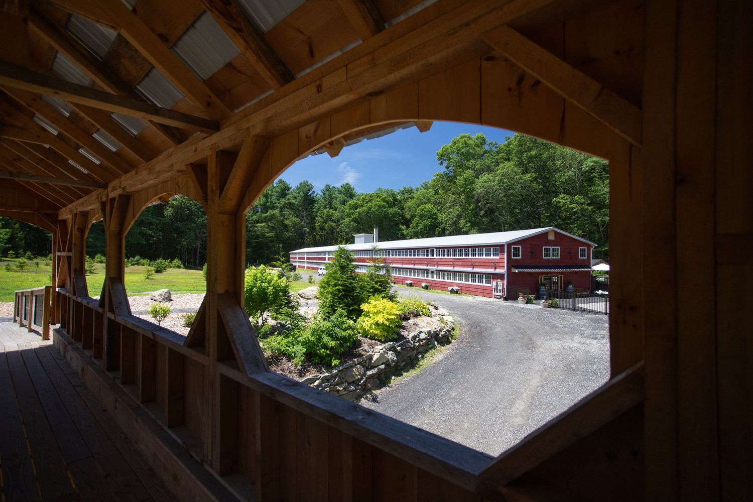 View through wooden covered bridge frame of a red barn building and lush green landscape on a sunny summer day.