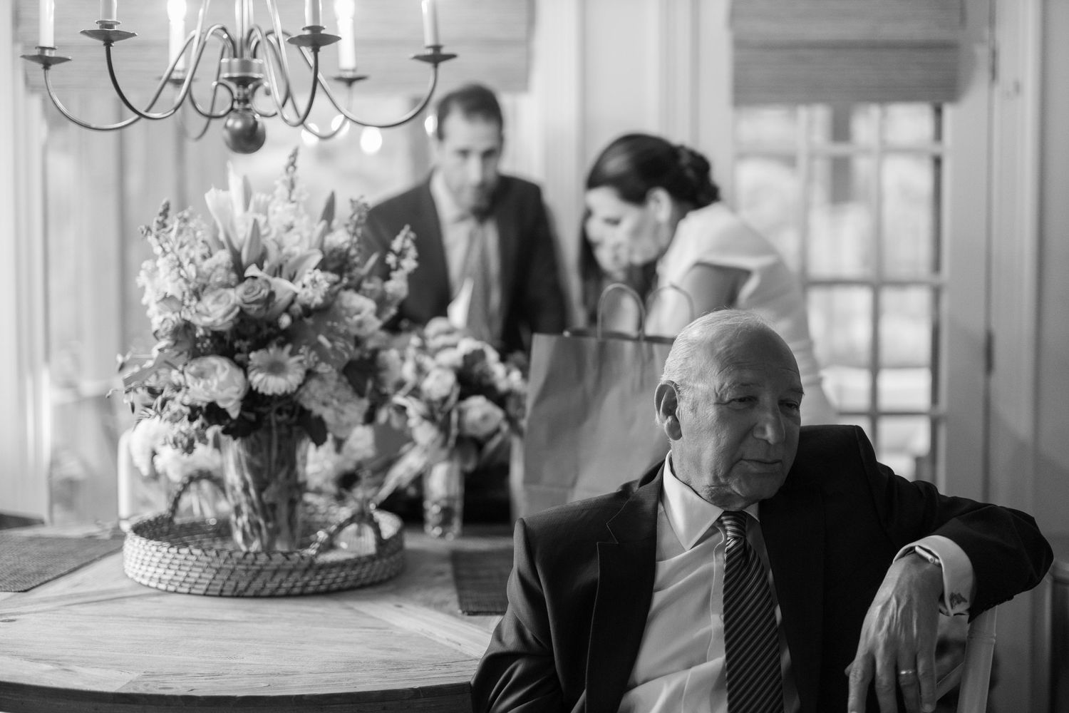A black and white photo series showing candid moments at a wedding reception with guests and floral decorations.