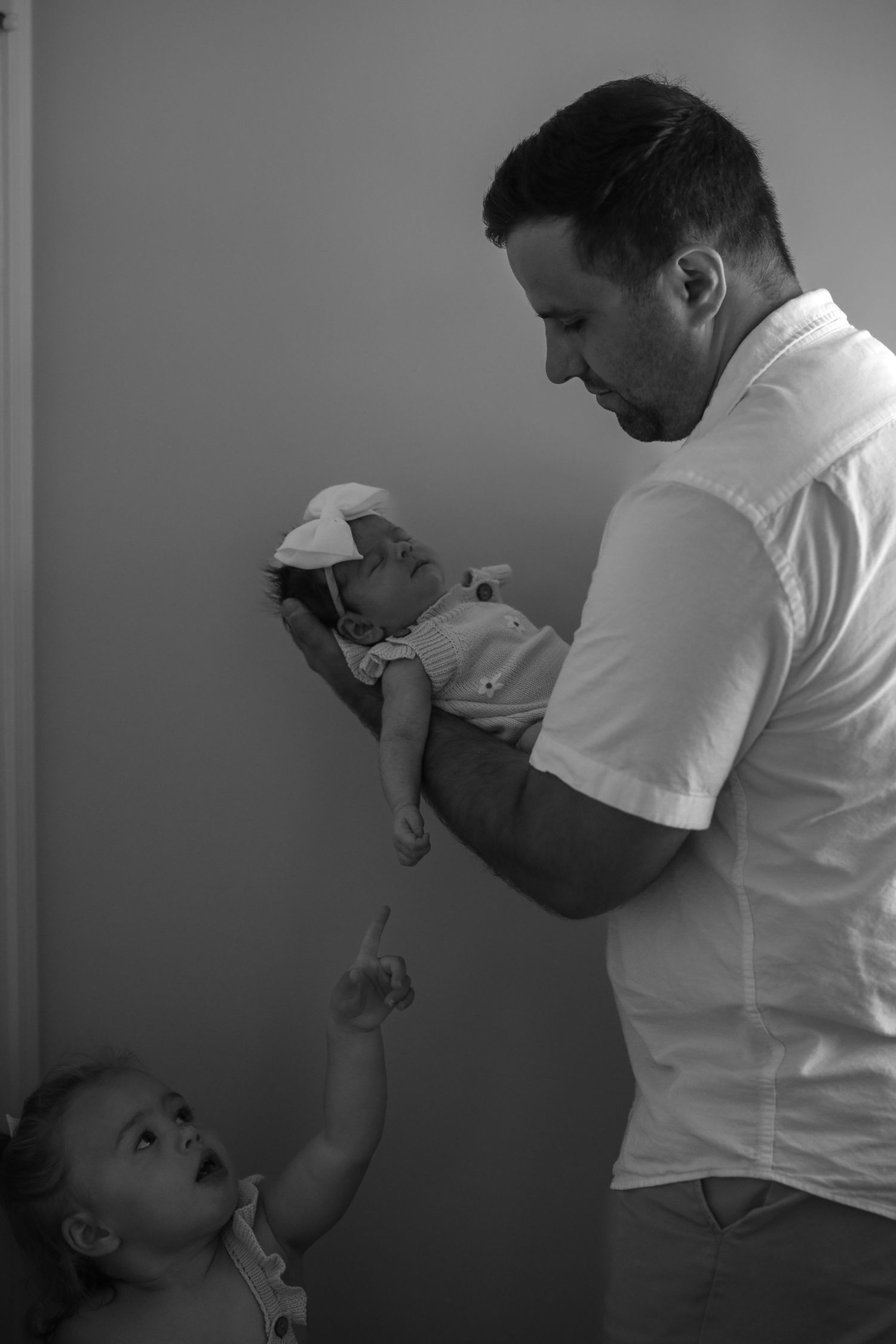black and white portrait of a father holding his newborn baby. His daughter reaches up to hold babys hand.