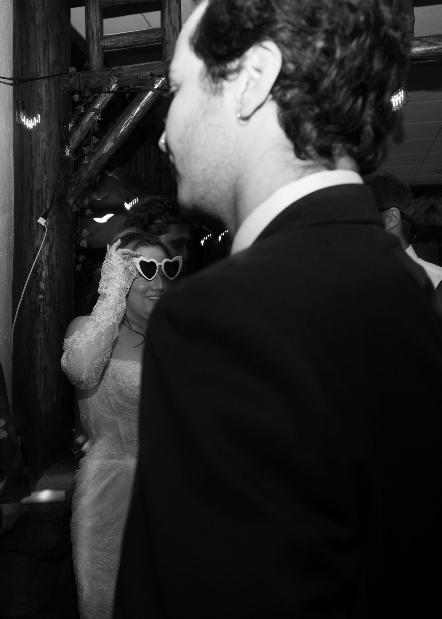 Black and white photo showing a couple dancing at a wedding reception with heart-shaped sunglasses.