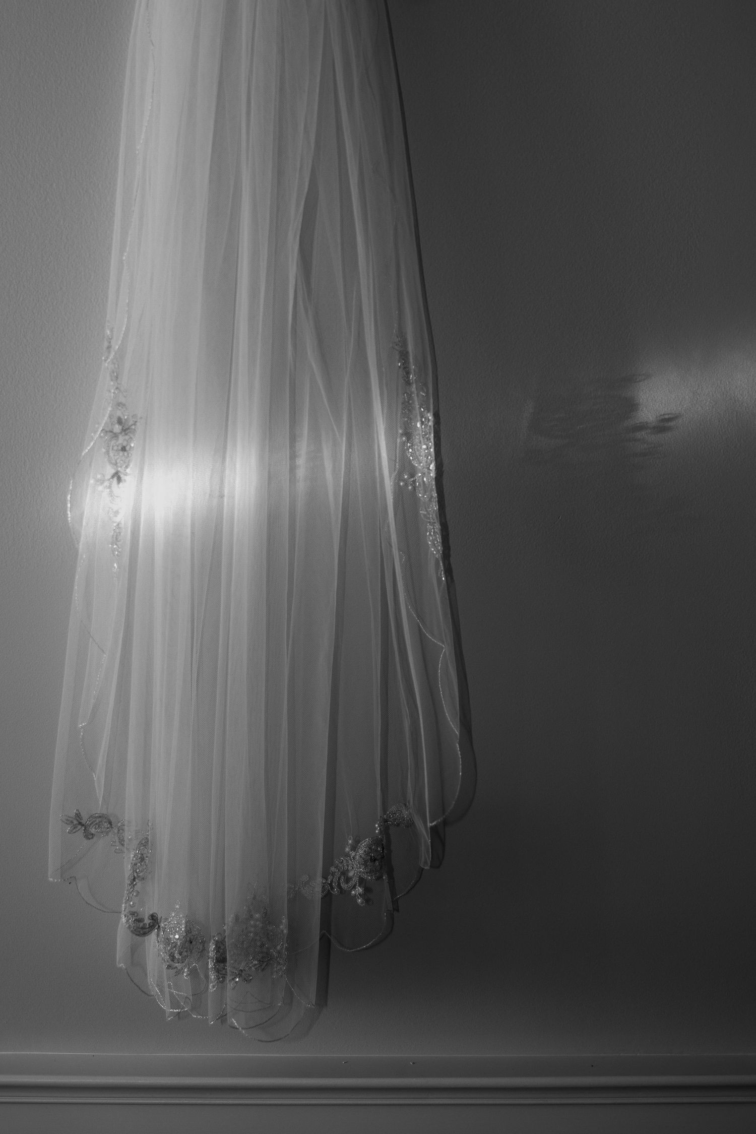 A close-up view of a white wedding veil with delicate lace details hanging in soft lighting.