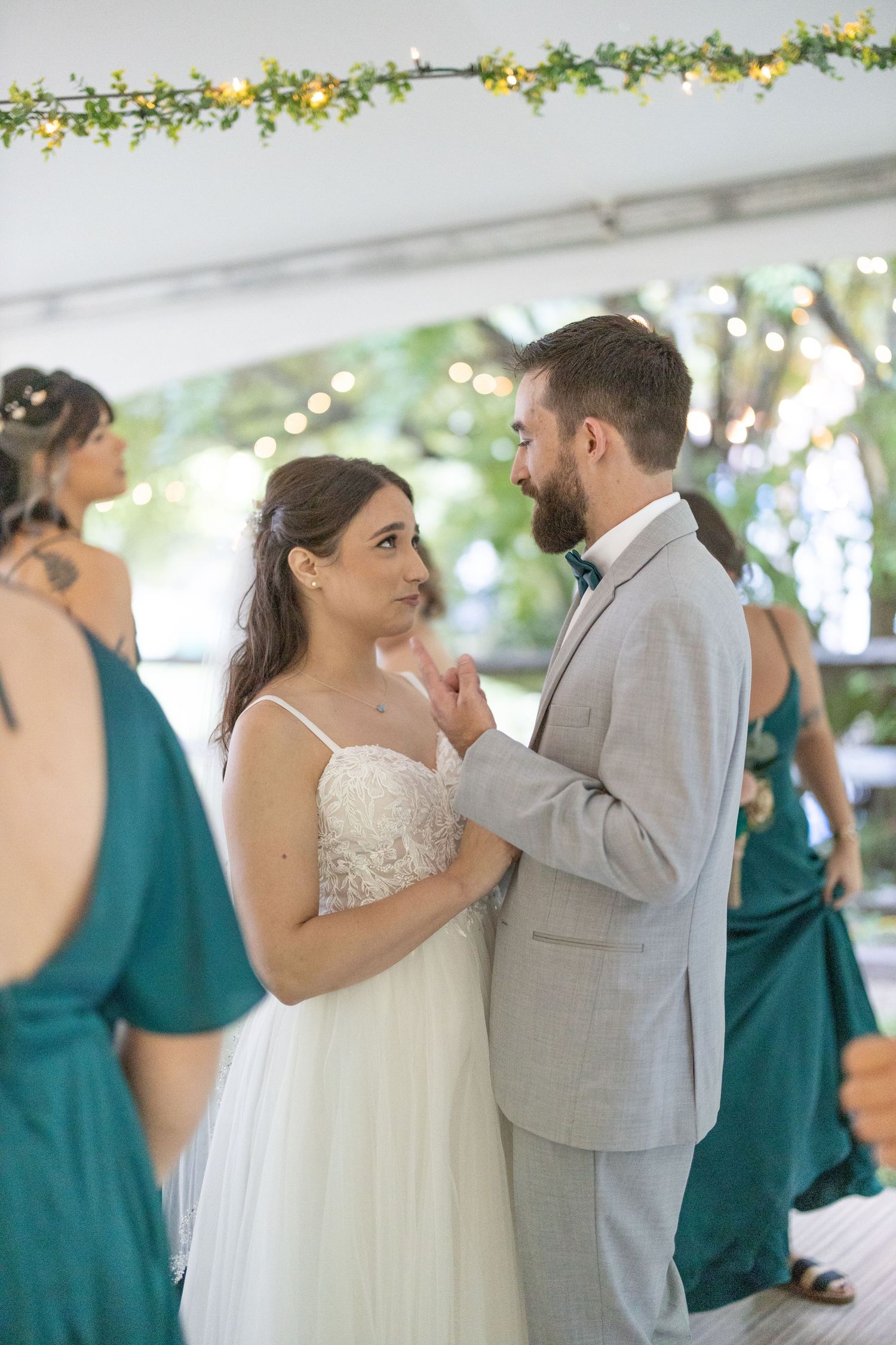 A couple shares their first dance at a wedding reception under floral decorations with bridesmaids in teal dresses nearby.