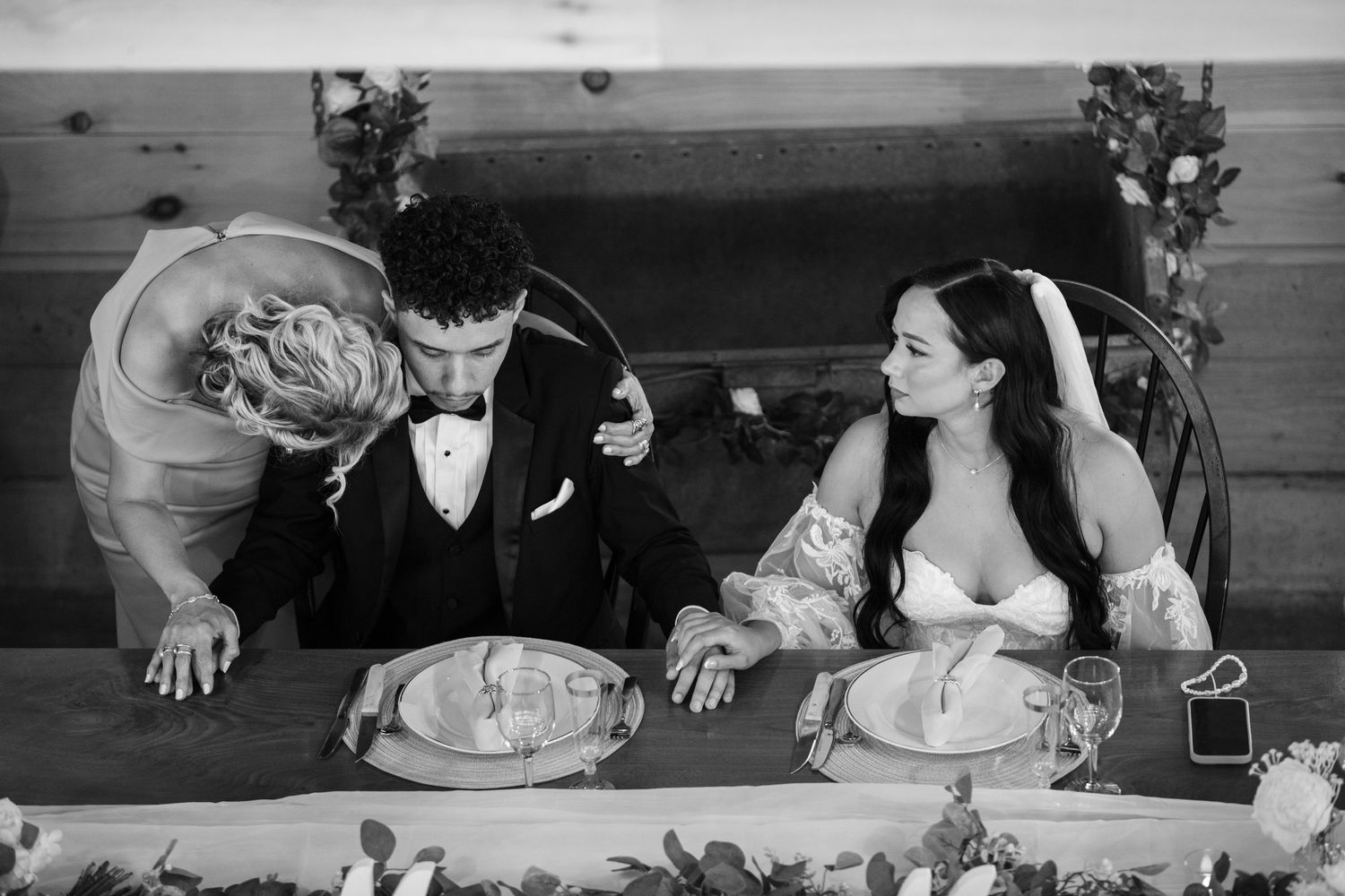 Black and white portrait of couple praying before dinner at their wedding.