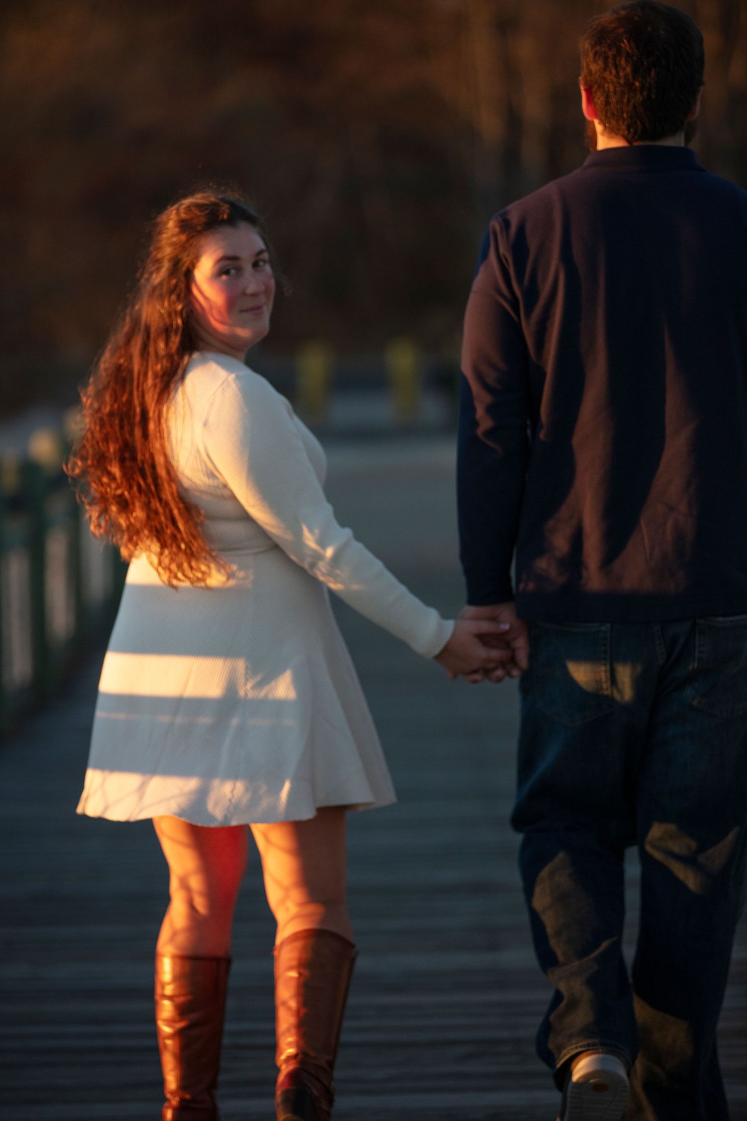 A couple walking on a wooden dock at sunset with warm golden light illuminating their silhouettes.