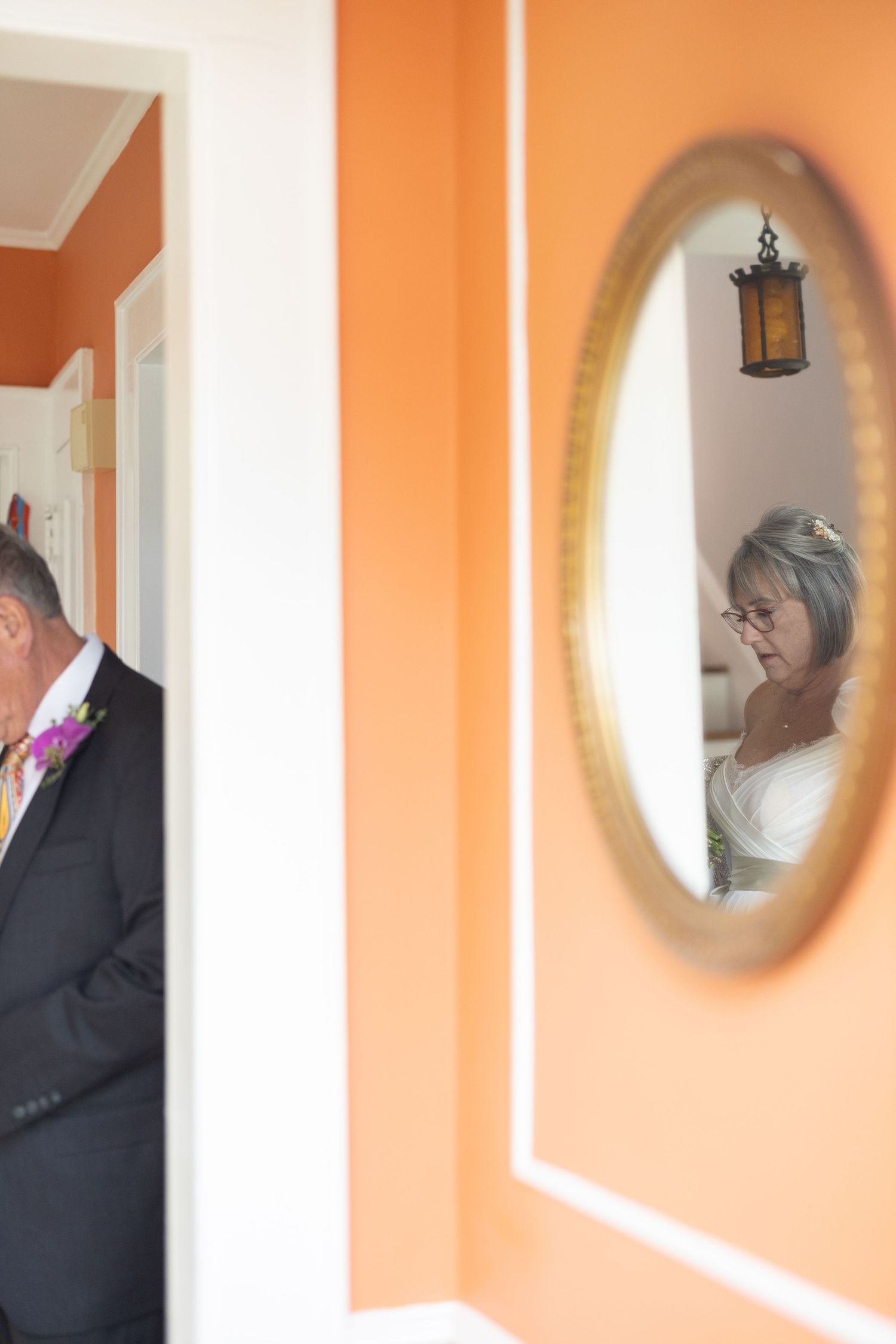 Four sequential photos show a couple in formal attire reflected in oval mirrors mounted on a peach-colored wall.