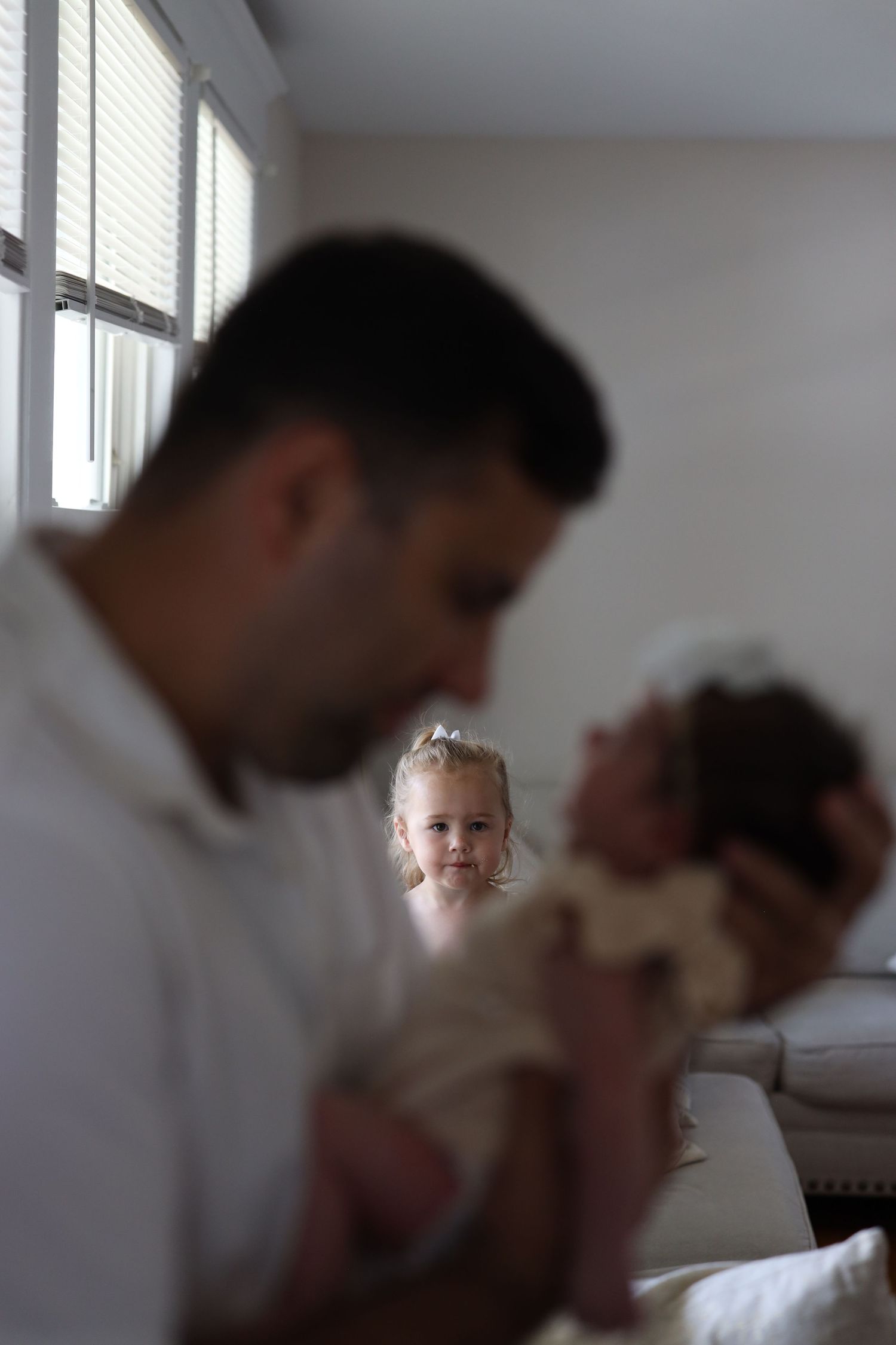 Candid portrait of a father holding his newborn in focus. background shows younger sister.