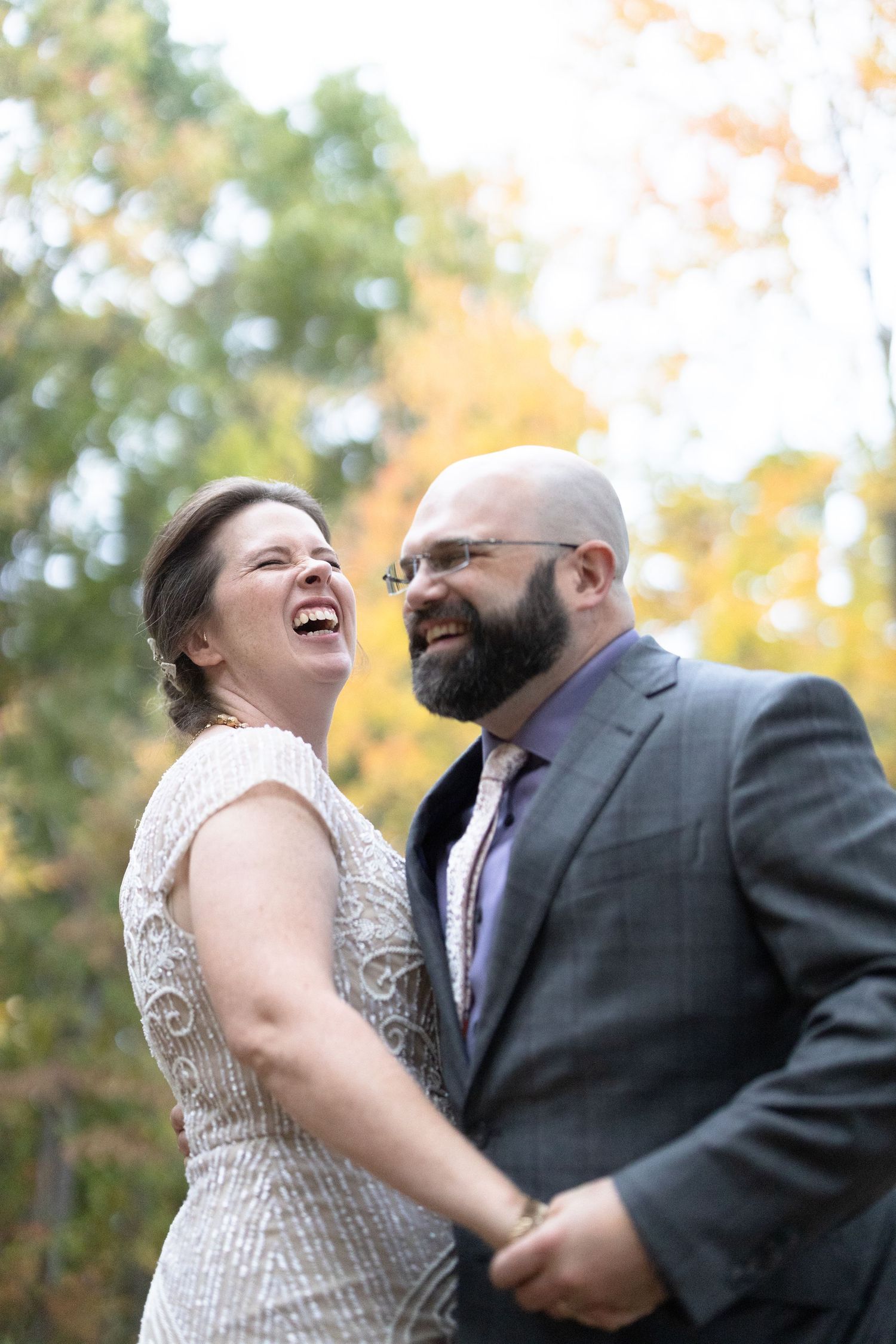 A couple shares a candid laughing moment together during an outdoor autumn wedding.