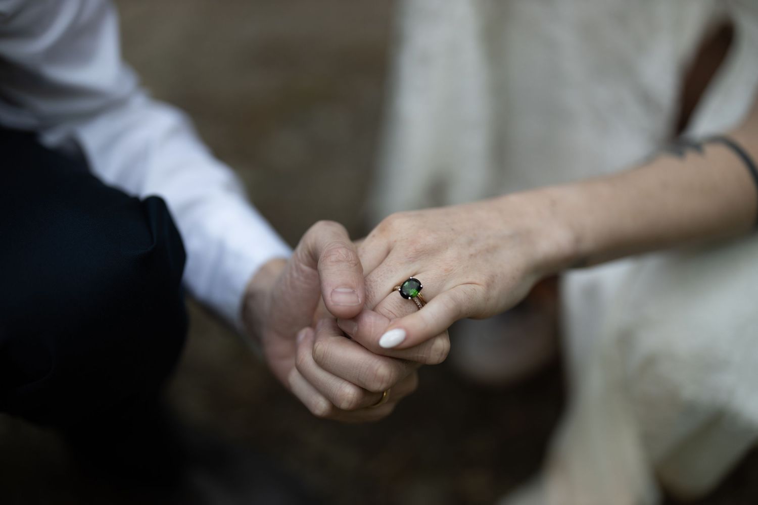 Close-up of two hands clasping together with an emerald ring visible on one finger. Elopement.