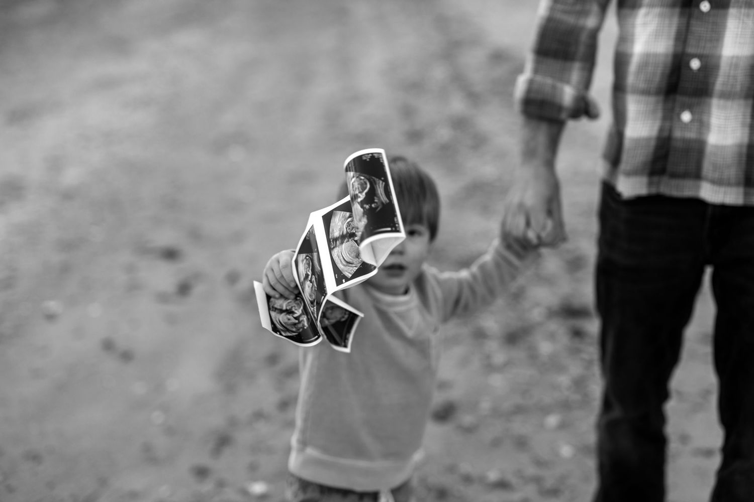 Child Holds ultrasound photo at the beach. Black and white. Candid Portrait.