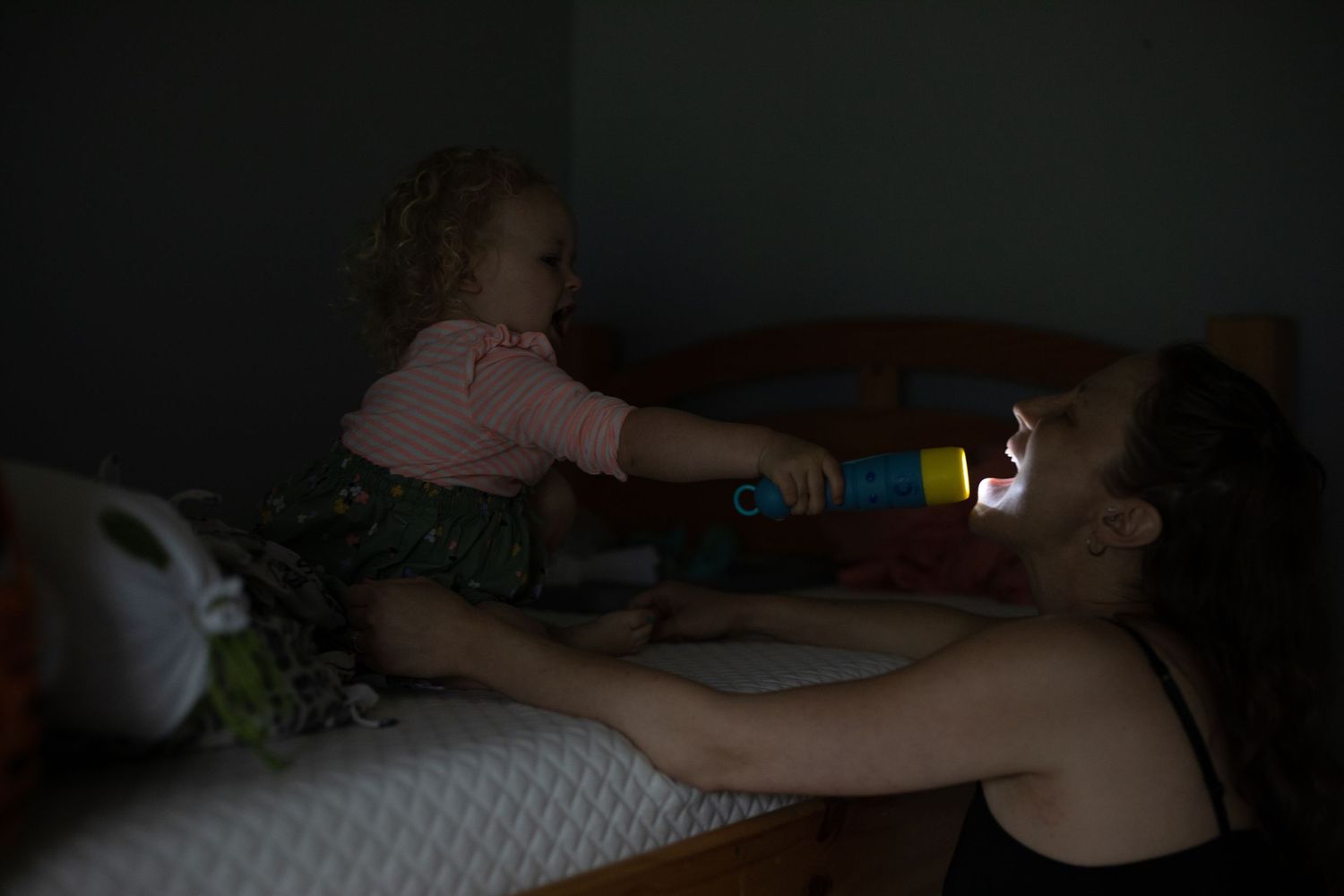 A child plays with a flashlight in a dark room while lying on her bed.