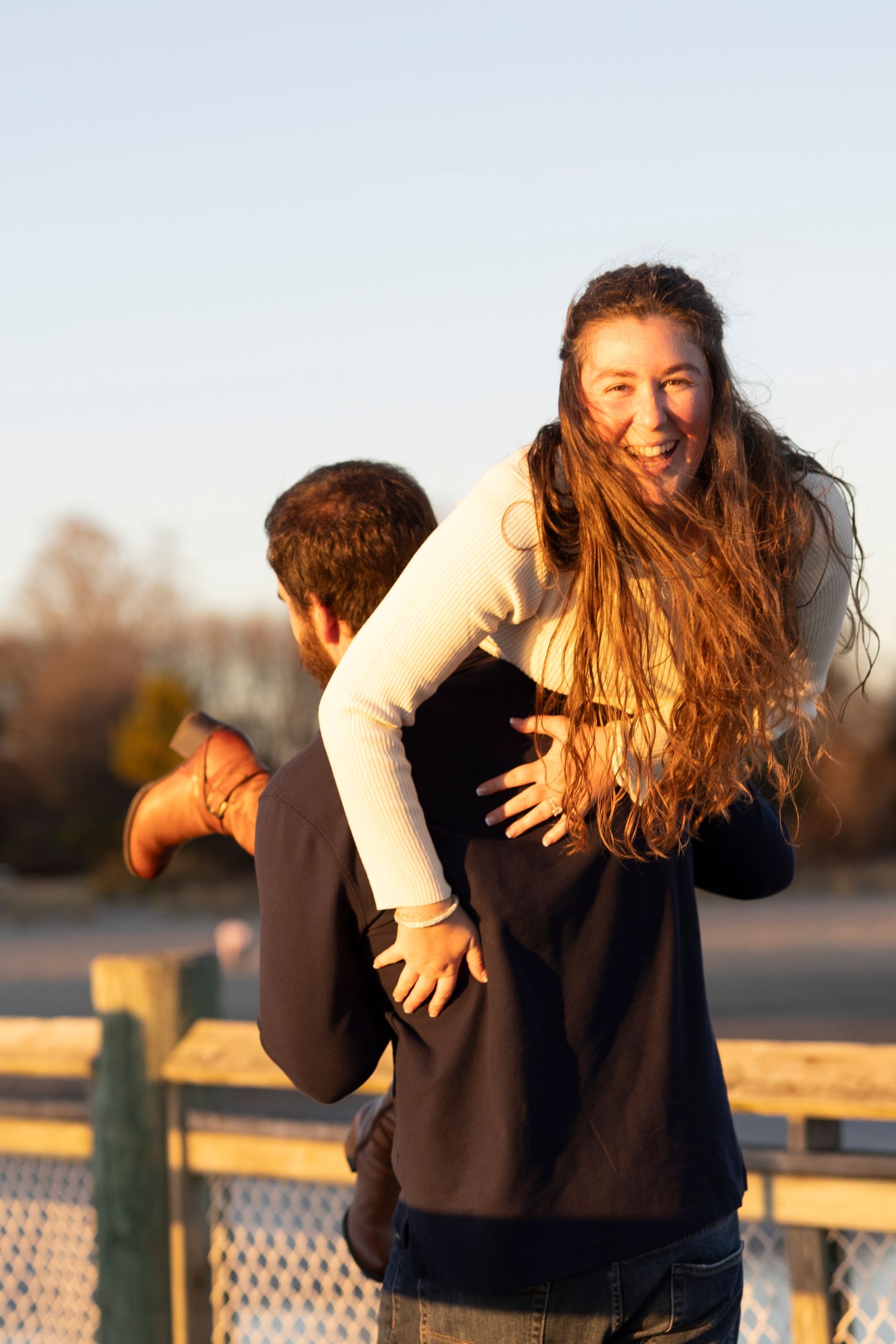A couple embraces and laughs together at sunset on a wooden deck by the water.
