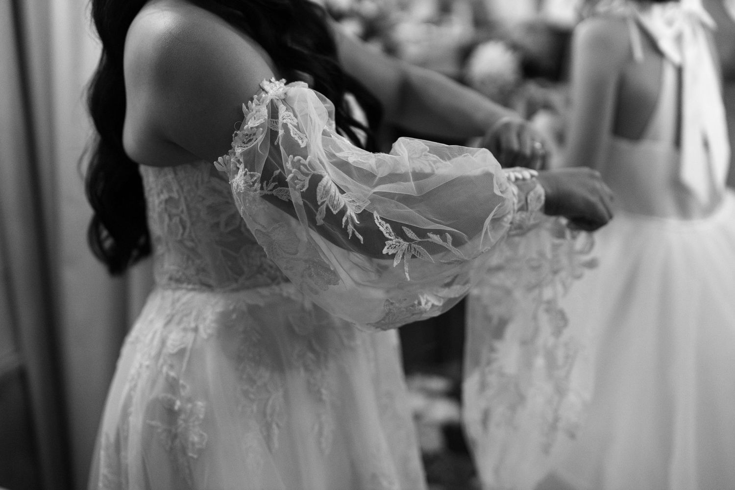 Portrait of a bride getting ready in the bridal suite. Putting on the sleeves of her dress.