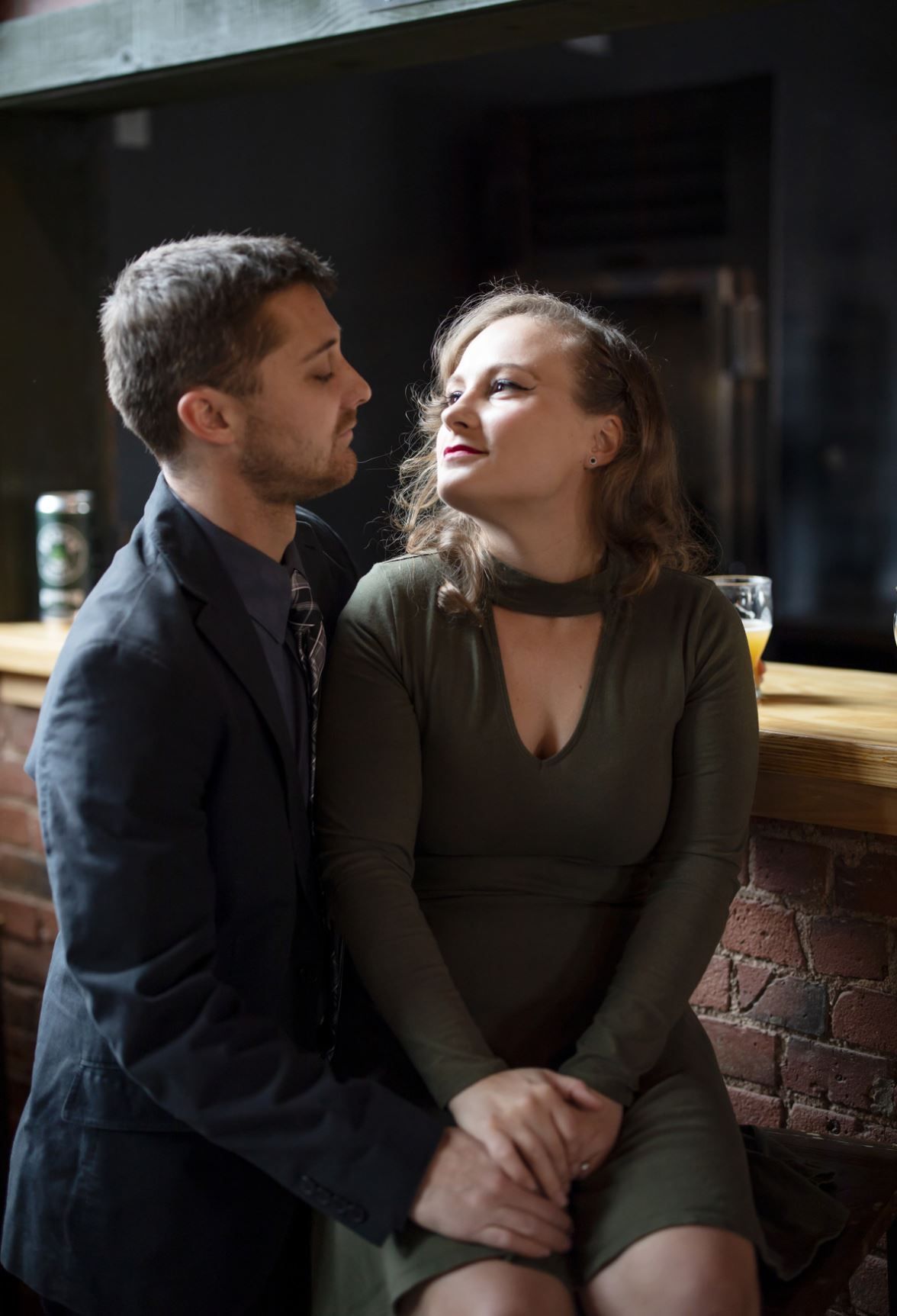 A couple shares an intimate moment together in a dimly lit room with exposed brick walls.