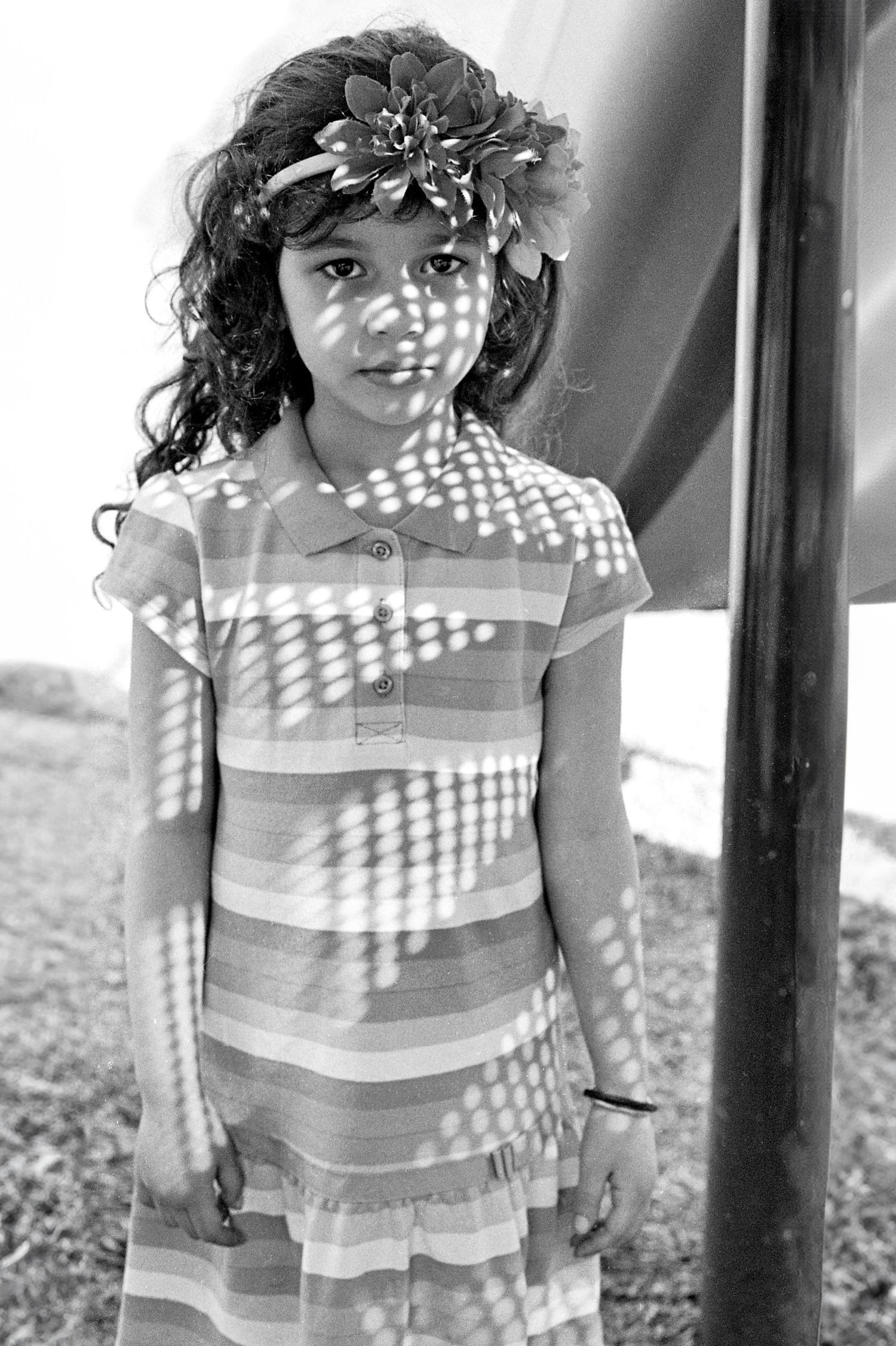 child in a striped dress sunlight creating shadow patterns. 35mm black and white film.