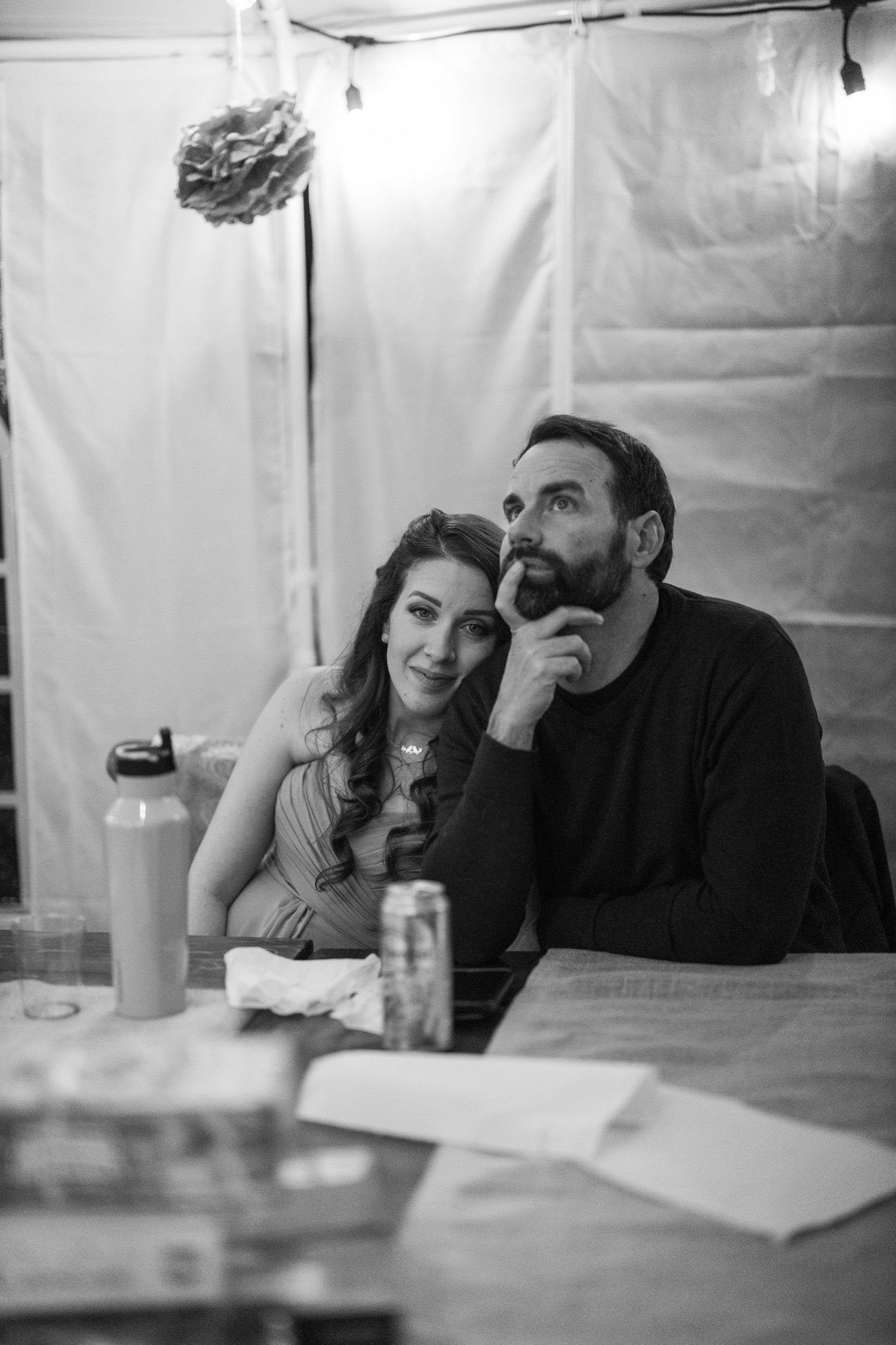 A couple sits together at a table in black and white, sharing an intimate conversation over drinks.