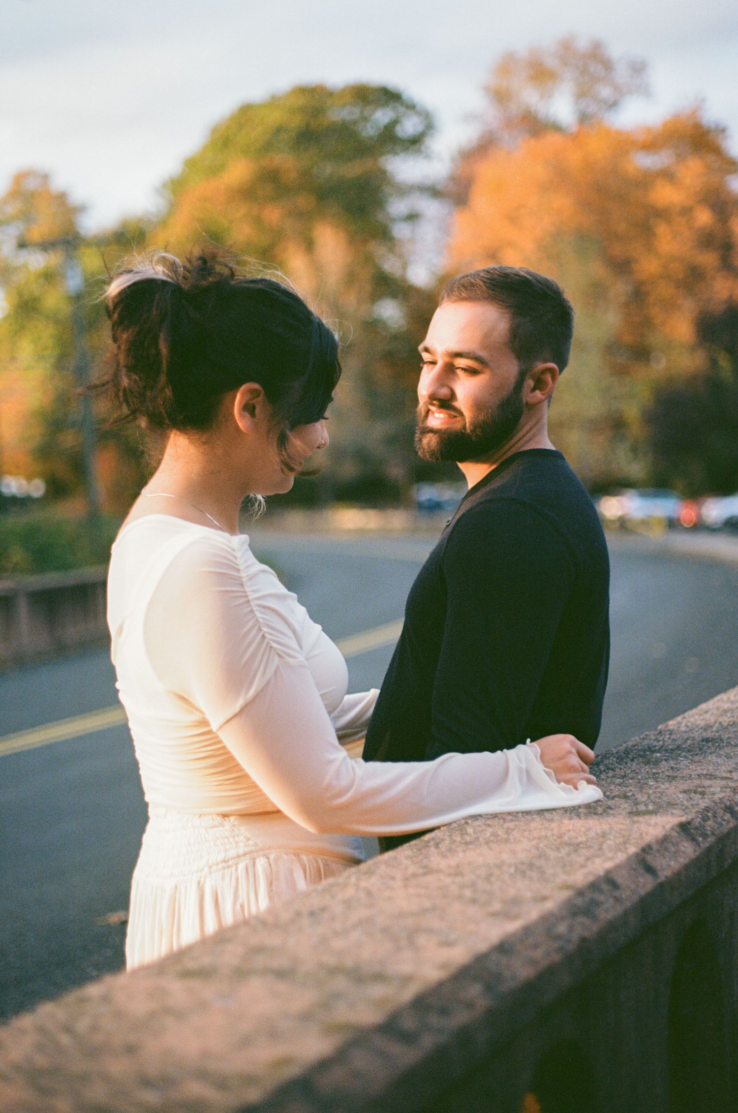 Couple in wedding attire sharing a romantic moment on a bridge surrounded by autumn foliage.