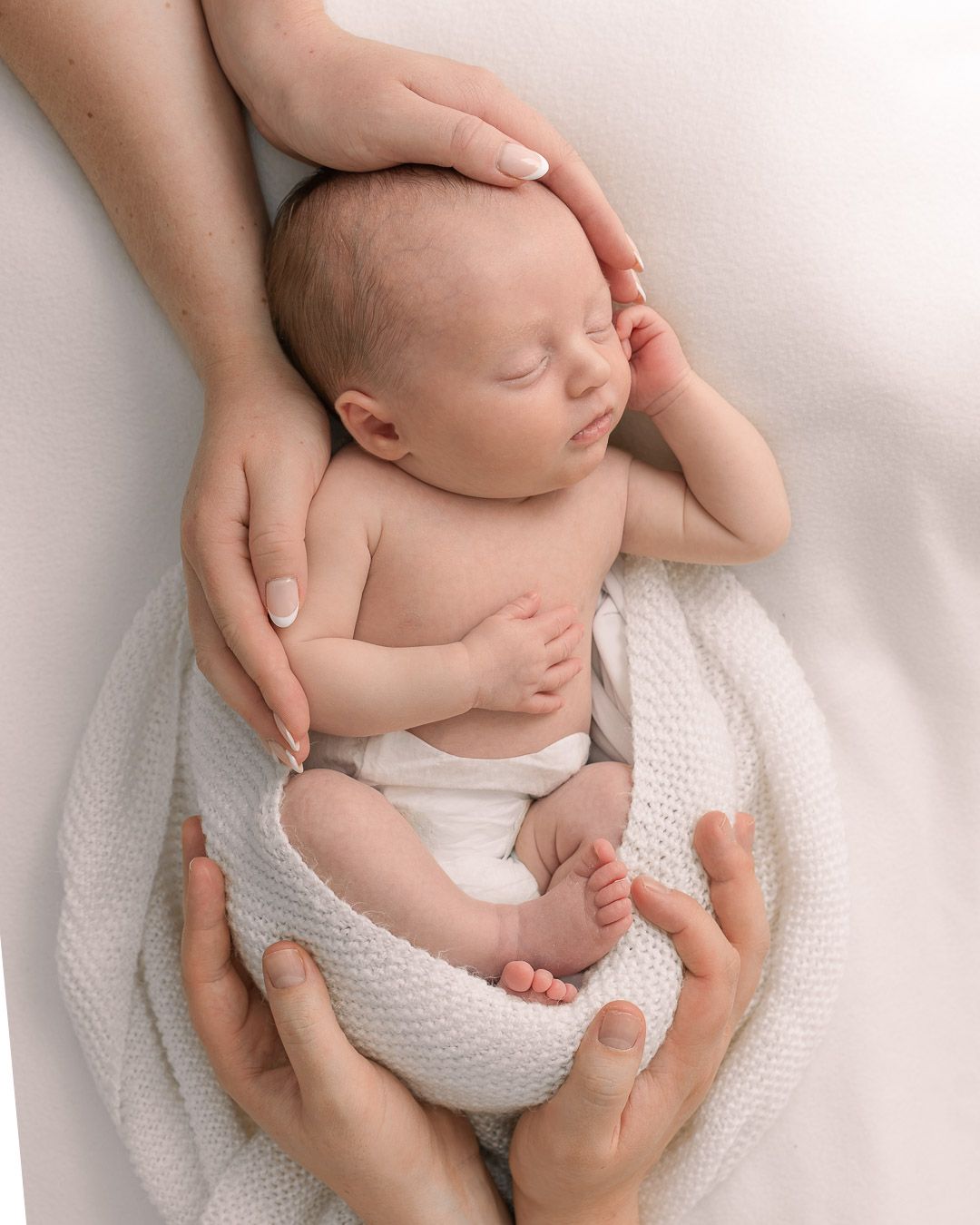 Mother and father's hands embracing their newborn sleeping on a home visit photo session in Walton, Chesterfield.