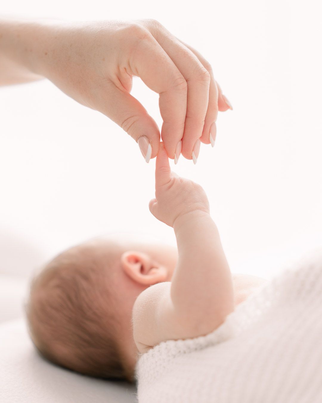 a mother holding a newborn baby's finger during a photo shoot done at the client's house in Chesterfield.