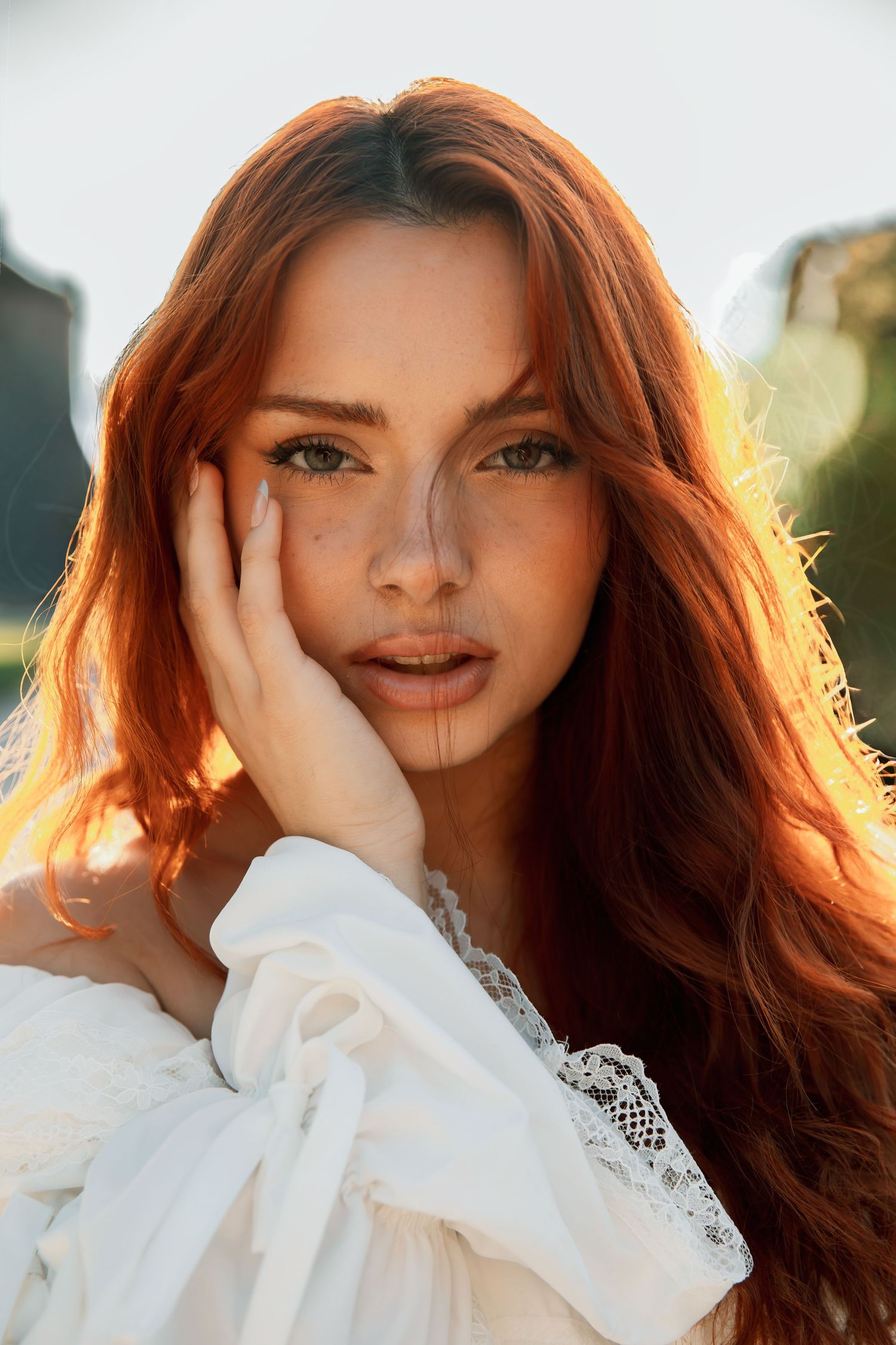 Portrait of a stunning redhead woman with freckles in a white lace dress at golden hour.
