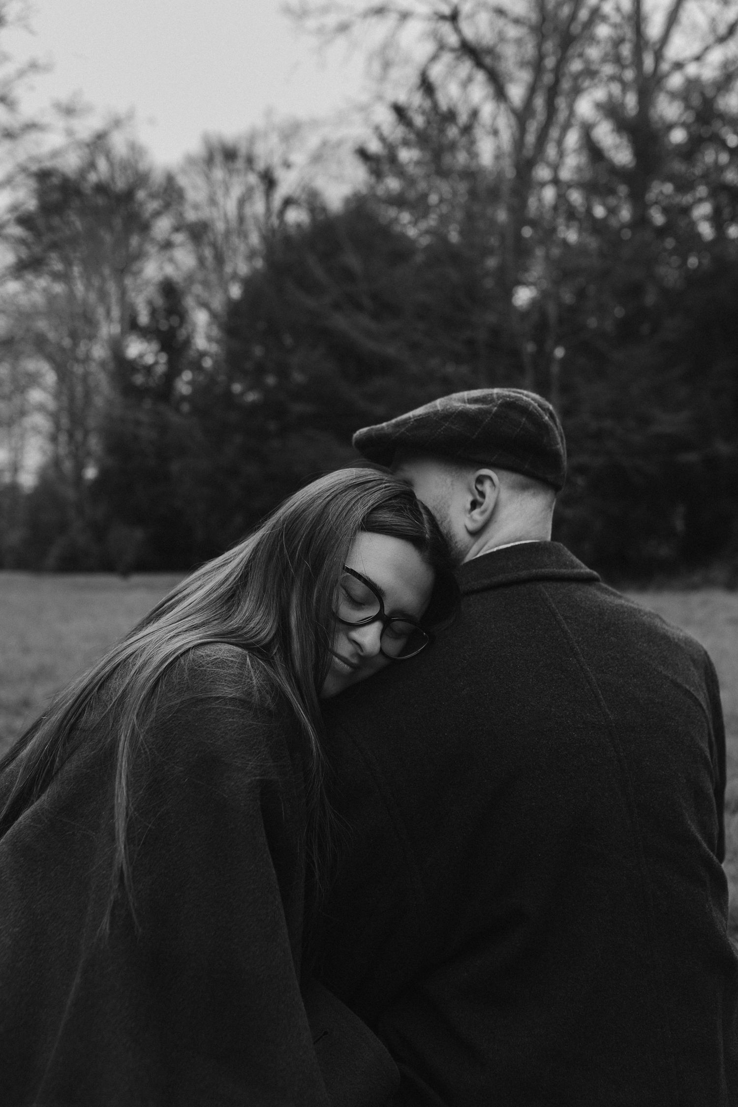 Black and white photo of woman resting her head on mans shoulder outdoors.