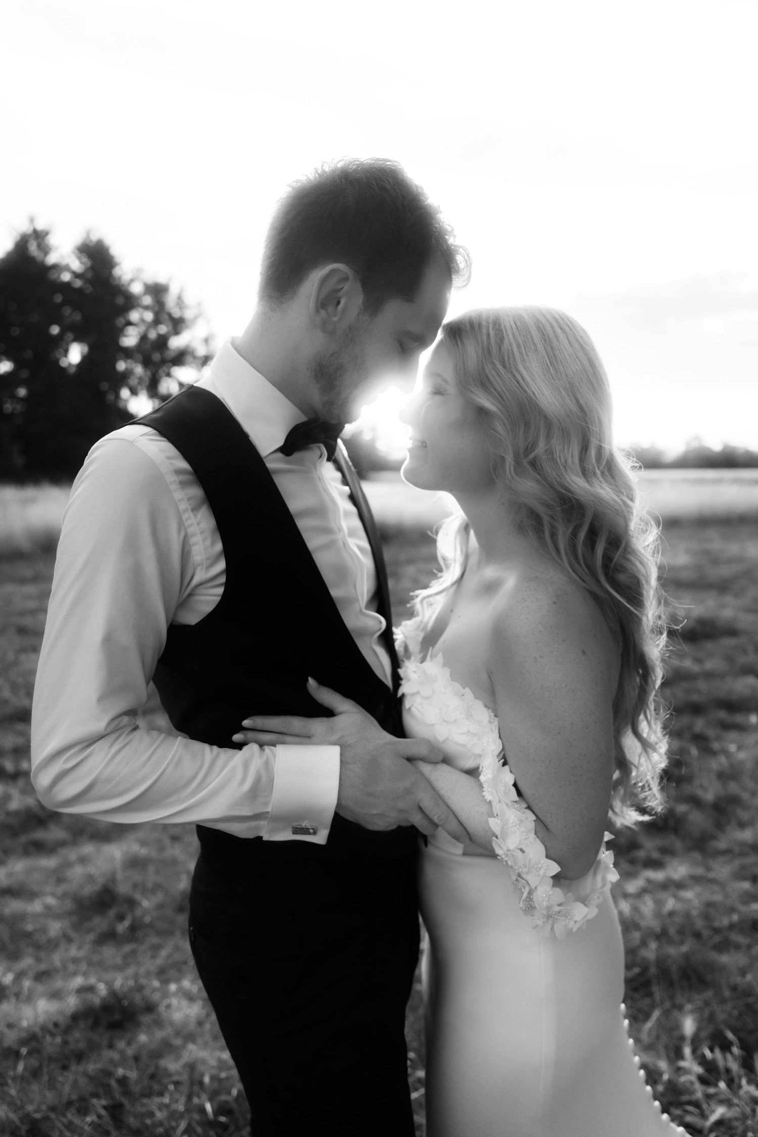 Black and white photo of a bride and groom sharing an intimate moment outdoors, backlit by golden sunset light.